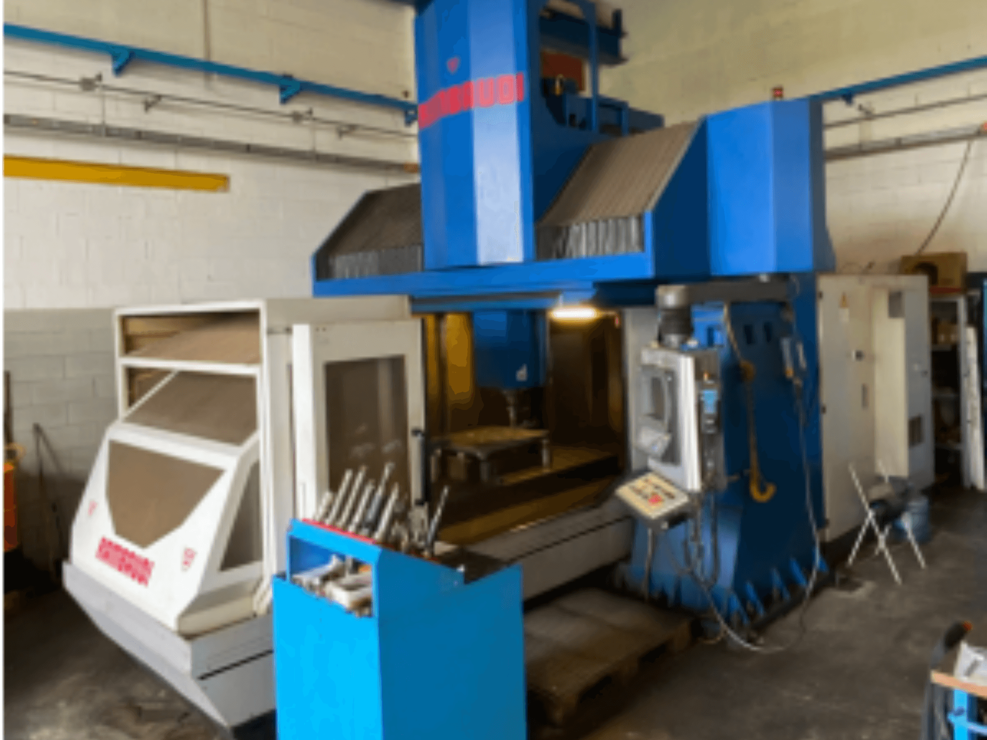 Вертикальный обрабатывающий центр Rambaudi RF103, вид спереди, показывающий органы управления, хранилище инструментов и зону обработки. Внешний вид сине-белого цвета.