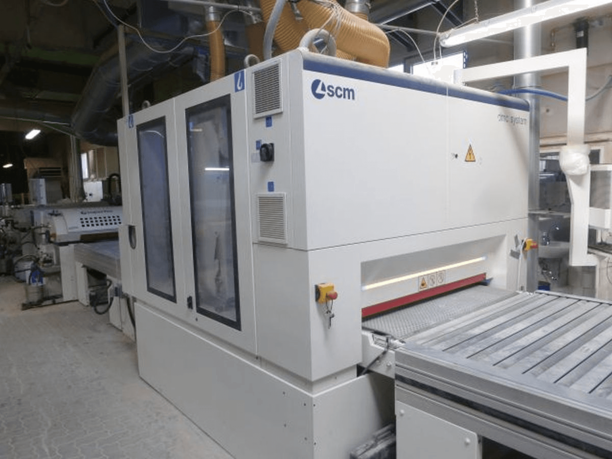 Ленточная шлифовальная машина SCM DMC SY TC 1350 в мастерской, вид сбоку, на котором видны панель управления и шлифовальная поверхность с элементами безопасности.