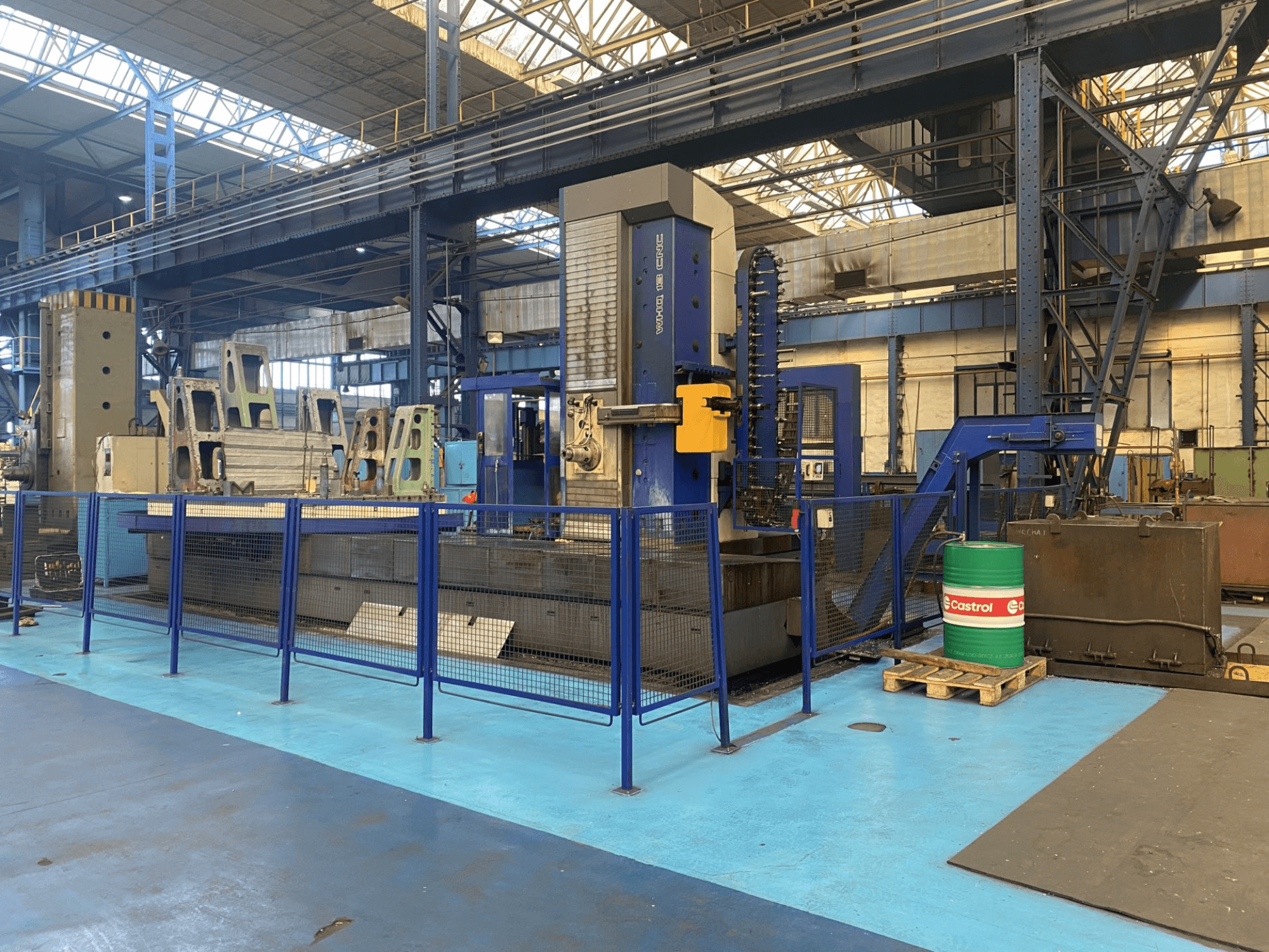 Расточной станок с ЧПУ TOS WHQ 13 в мастерской, вид спереди, видна синяя рама и окружающее защитное ограждение.