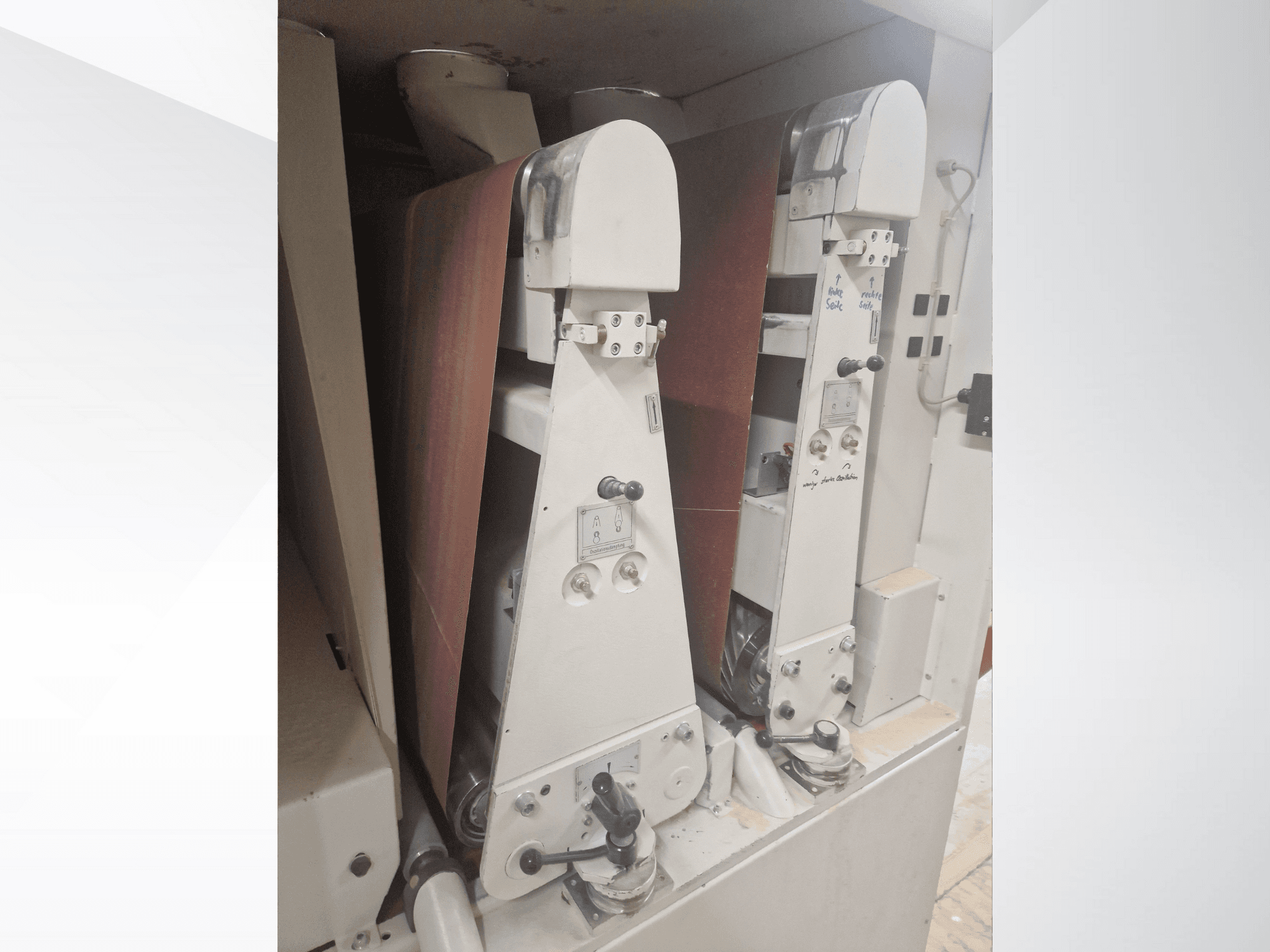 Два промышленных шлифовальных станка с красными шлифовальными лентами, вид спереди, видны элементы управления и металлические детали.