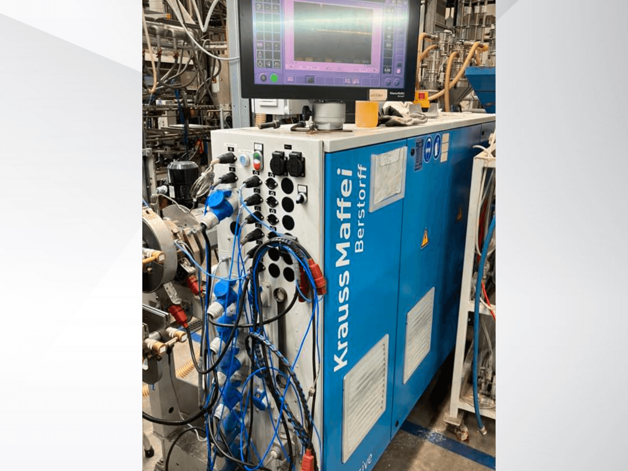 Промышленная машина Krauss Maffei Berstorff с панелью управления и монитором, с различными кнопками и подключенными шлангами, вид сбоку.