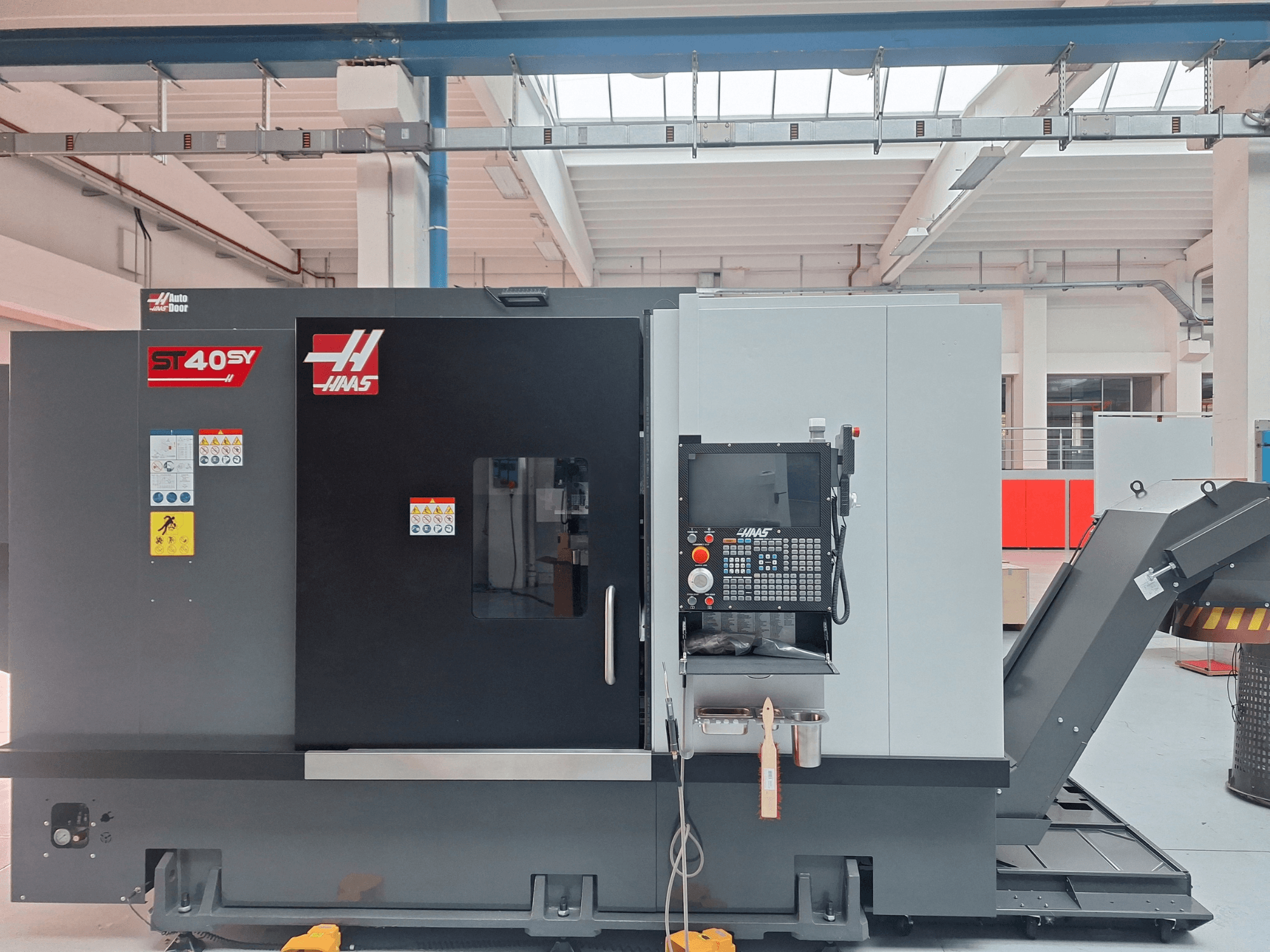 Горизонтальный токарный станок Haas ST-40SY в виде сбоку, на котором видны панель управления и предупреждающие надписи.