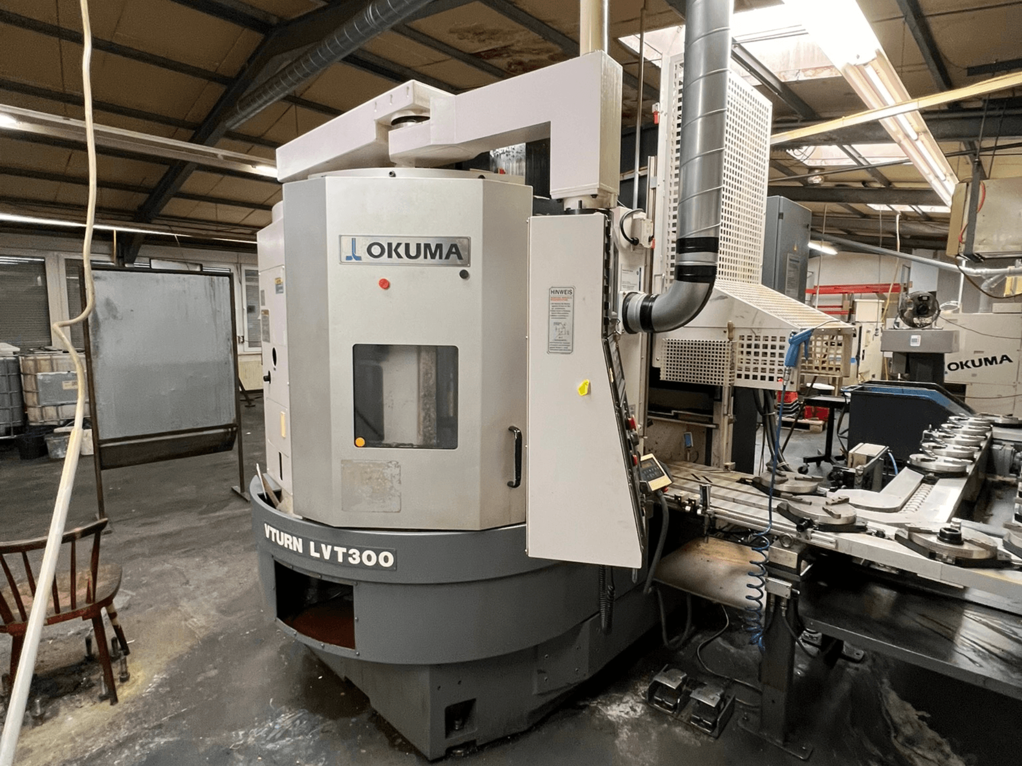 Токарный станок с ЧПУ Okuma Vturn LVT300, вид сбоку в промышленных условиях, демонстрирует панель управления и систему подачи СОЖ.