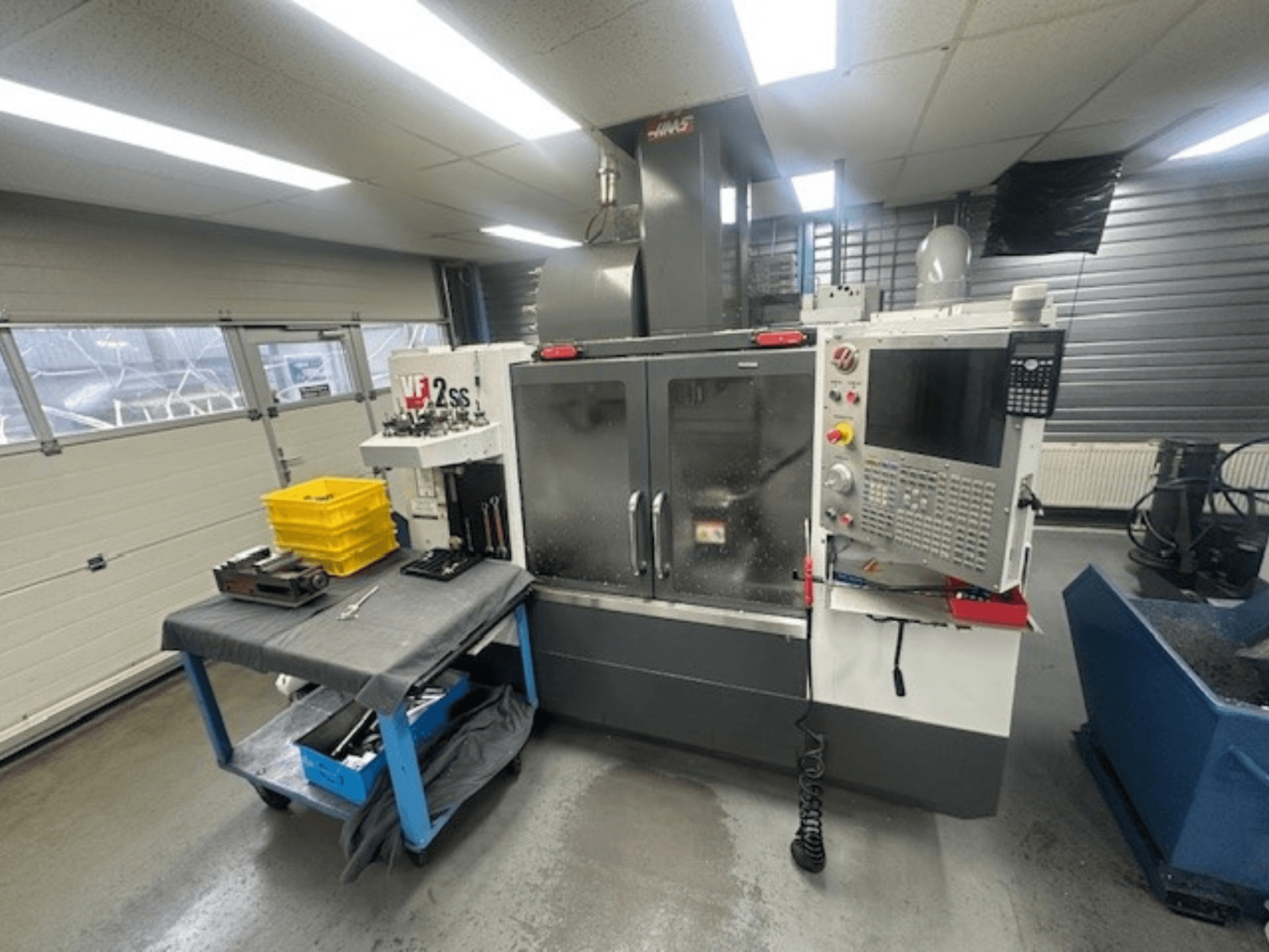 Вид спереди вертикального обрабатывающего центра HAAS VF-2SS с панелью управления, рабочим столом и станком для хранения инструментов.