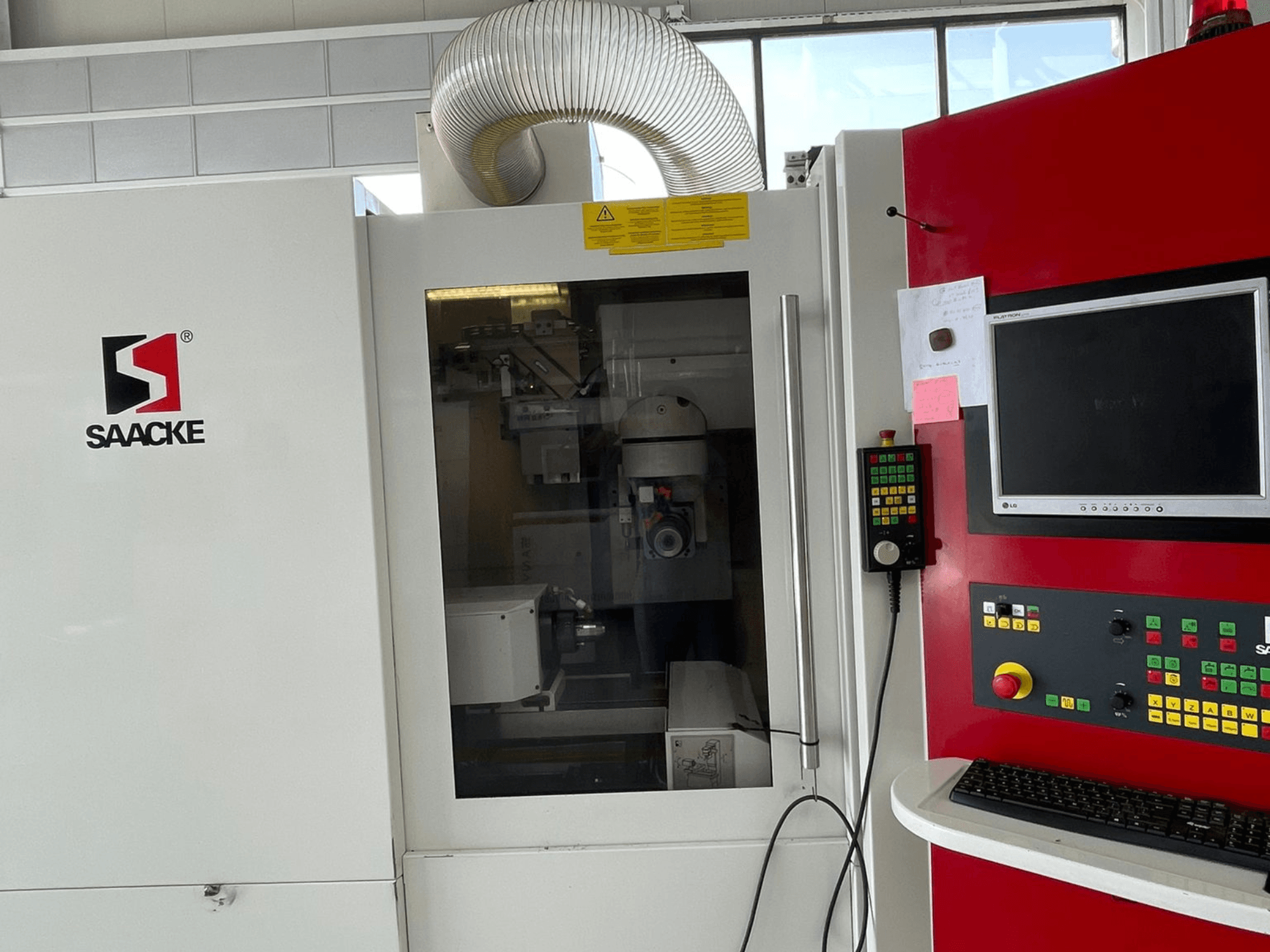 Машина SAACKE белого и красного цвета, вид спереди, панель управления, монитор и внутренние детали видны через стекло.
