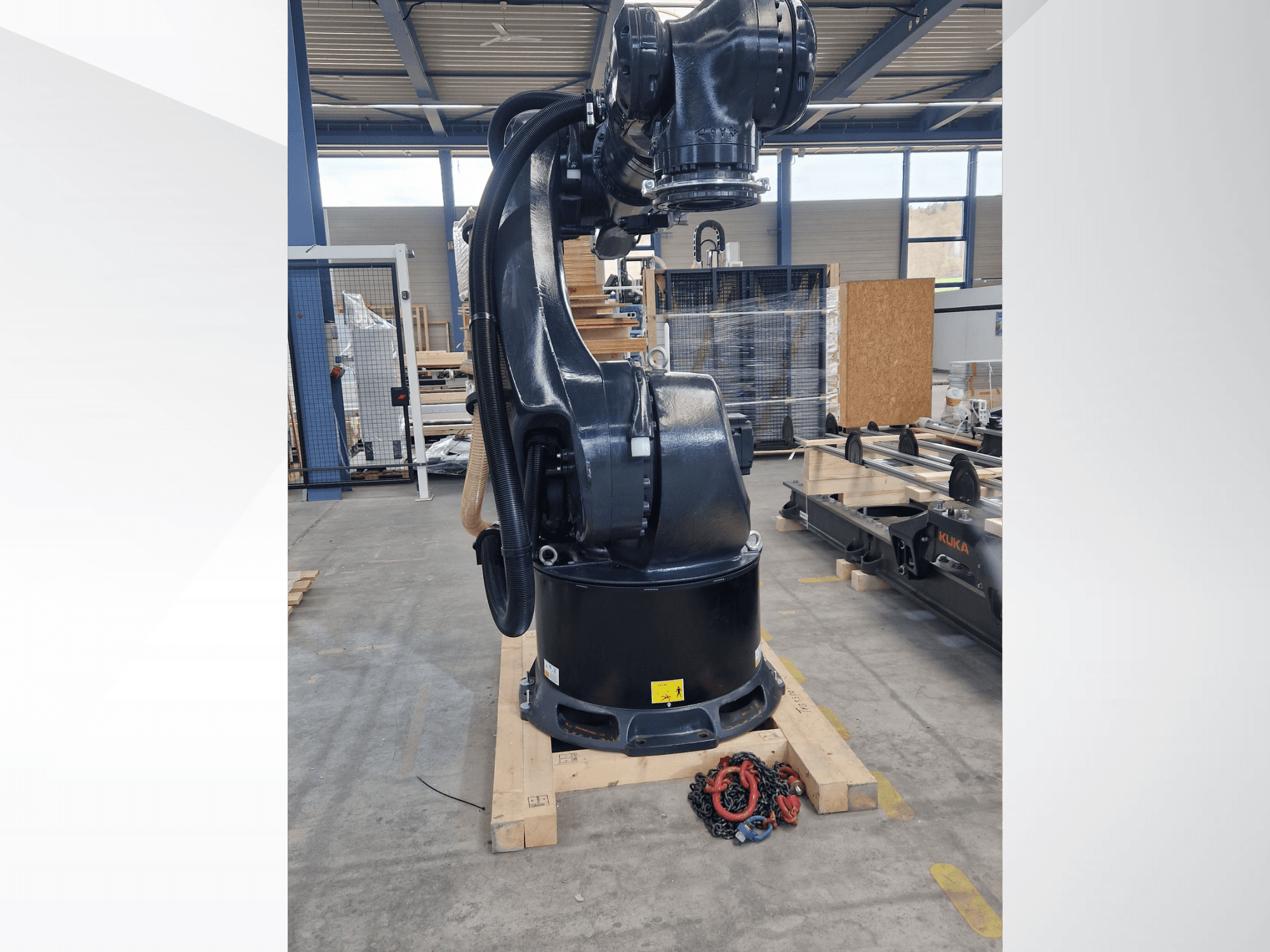 Роботизированная рука KUKA KR 340 R3330 на складе, вид сбоку, демонстрирующий её основание и кабели, на переднем плане — цепи.