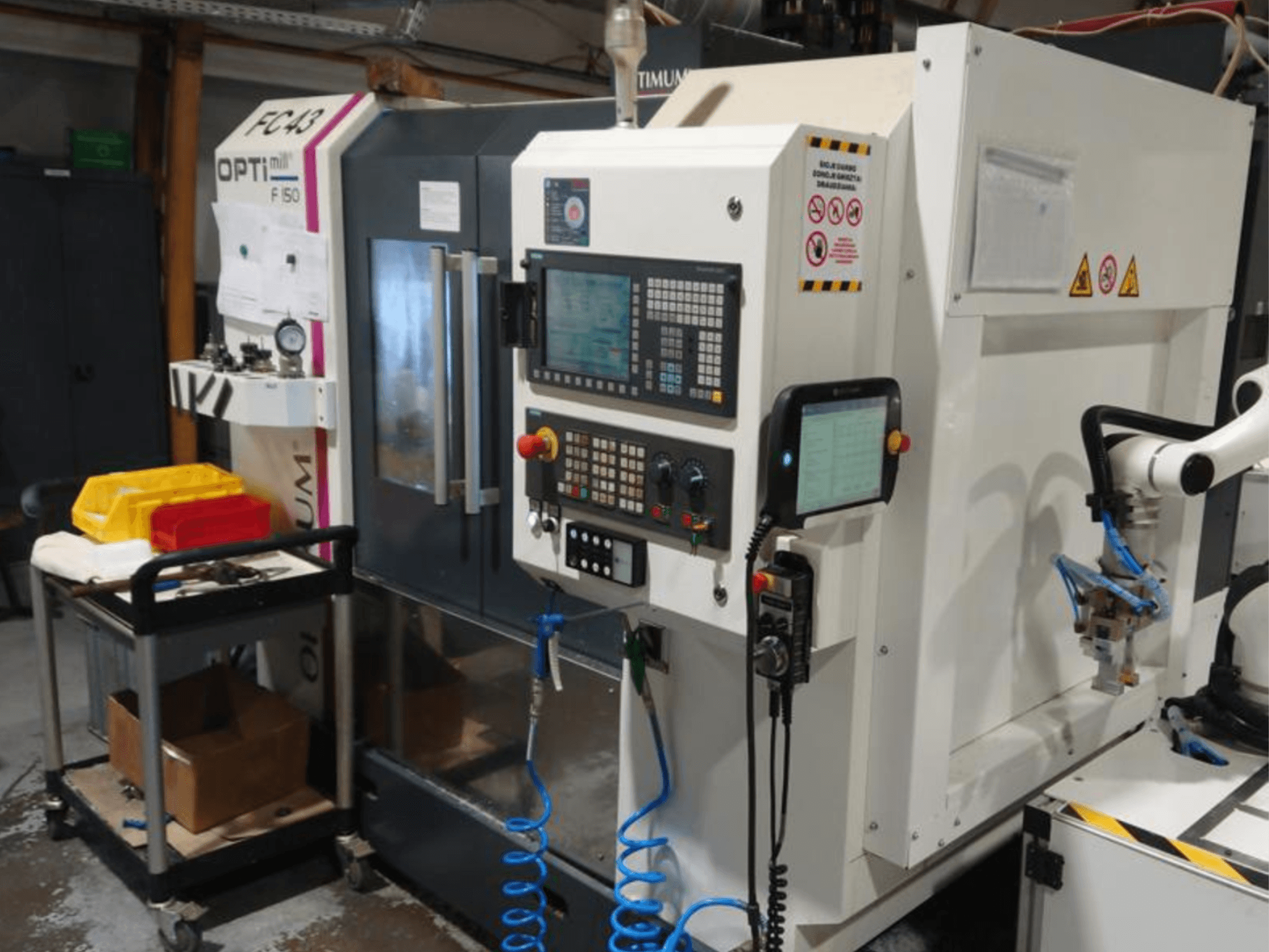 Панель управления фрезерного станка OPTIMUM F50 со шлангами, инструментами и роботизированной рукой в мастерской.