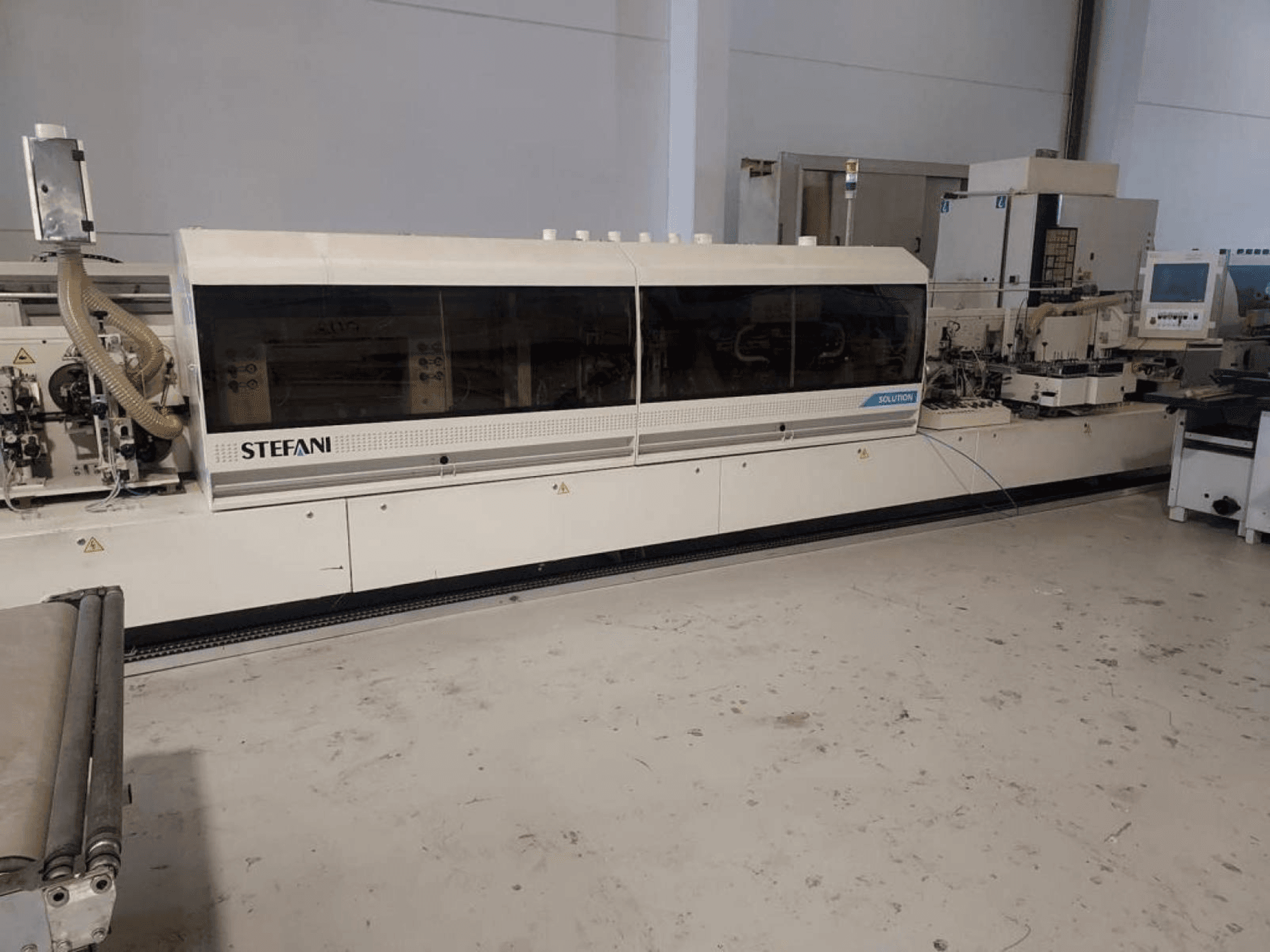 Кромкооблицовочный станок Stefani Solutions, вид спереди, с системой пылеудаления и панелью управления, в мастерской.