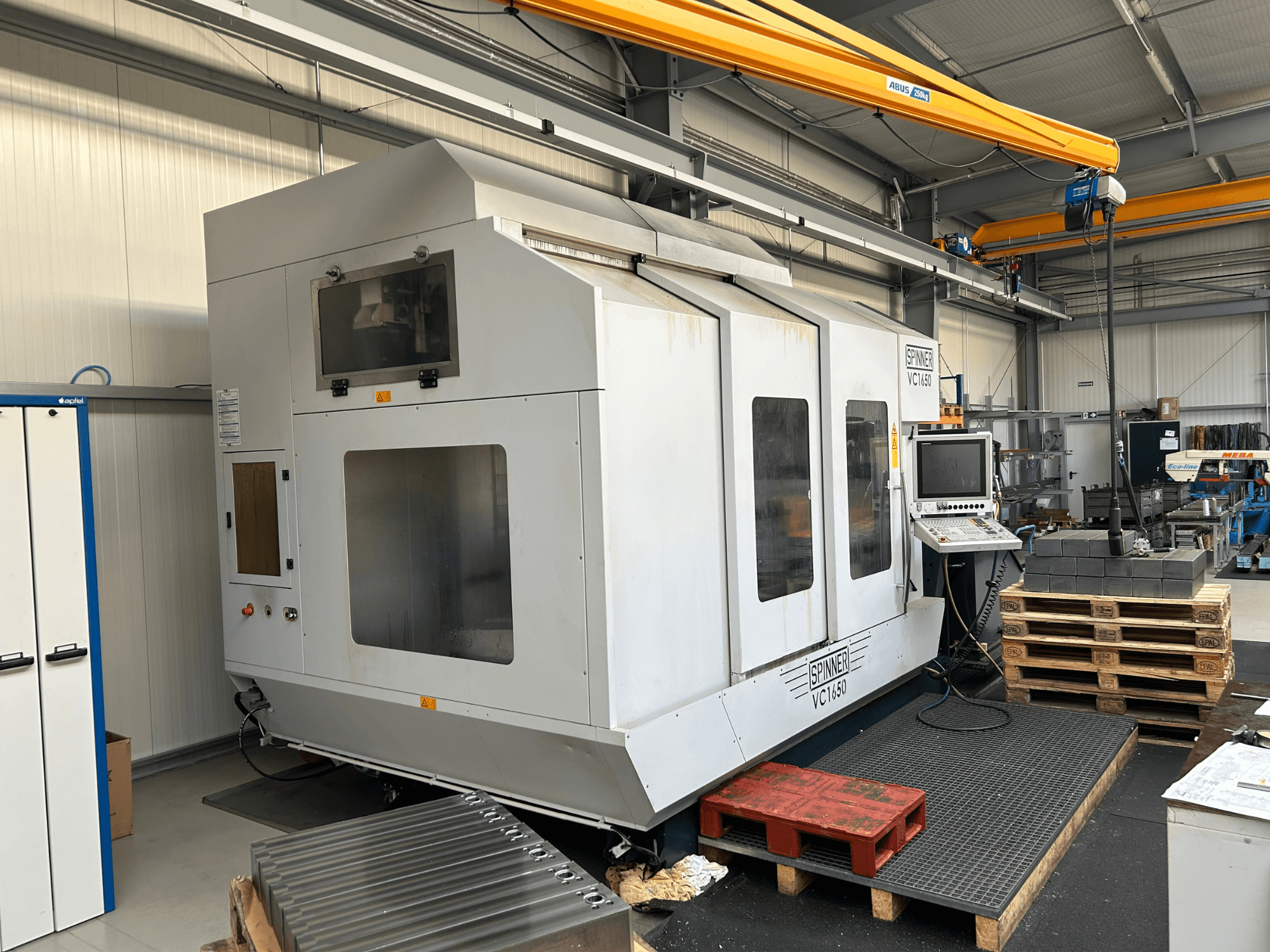 Станок с ЧПУ Spinner VC 1650, вид спереди, с панелью управления, большими окнами и паллетами, сложенными рядом в мастерской.