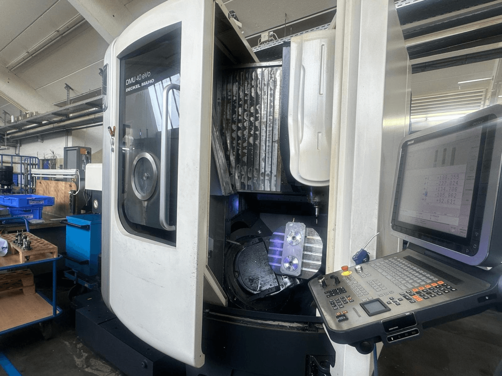 Фрезерный станок DMU 40 eVo фирмы Deckel Maho в мастерской, вид спереди, видна панель управления и металлическая деталь в шпинделе.