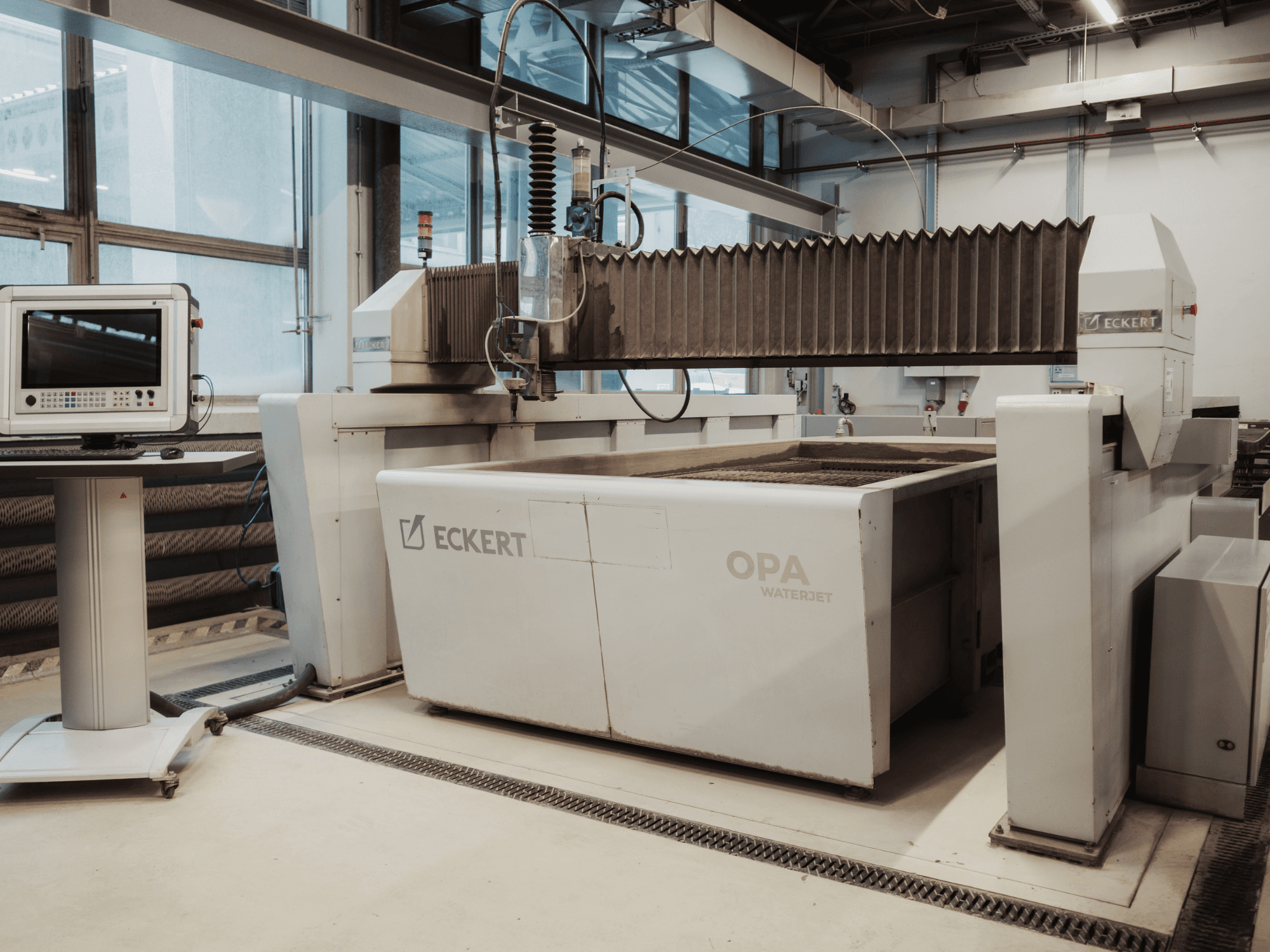 Машина для гидроабразивной резки ECKERT OPAL в цехе, вид спереди с расположенной рядом консолью управления.
