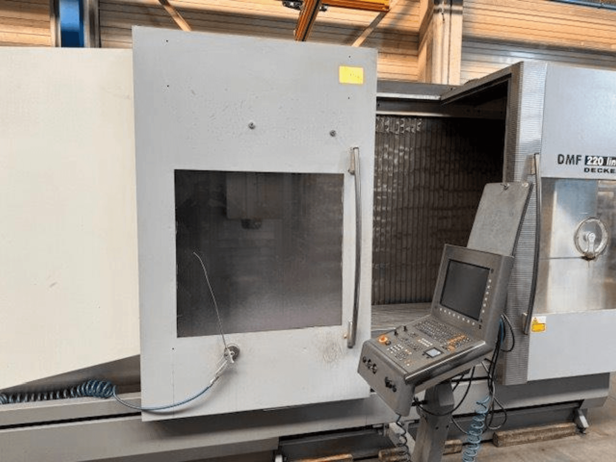 Вид спереди на вертикальный обрабатывающий центр DECKEL MAHO DMF 220 Linear, демонстрирующий панель управления и открытую дверь станка.