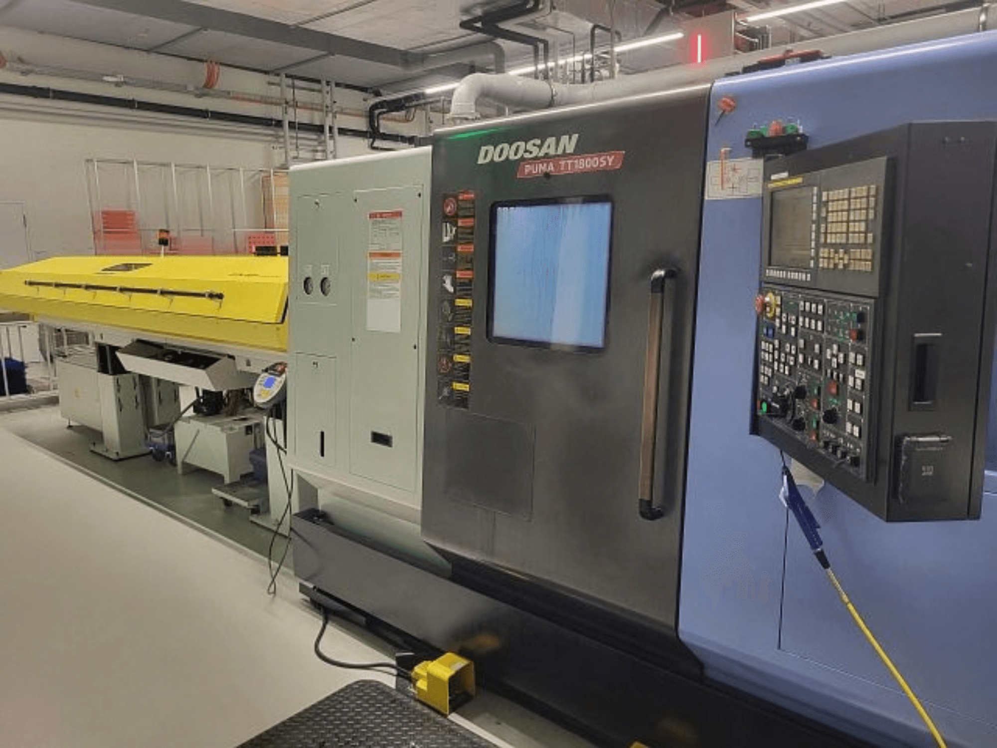 Токарно-фрезерный центр DOOSAN PUMA TT 1800 SY, вид спереди с панелью управления и желтым кожухом, промышленная обстановка.