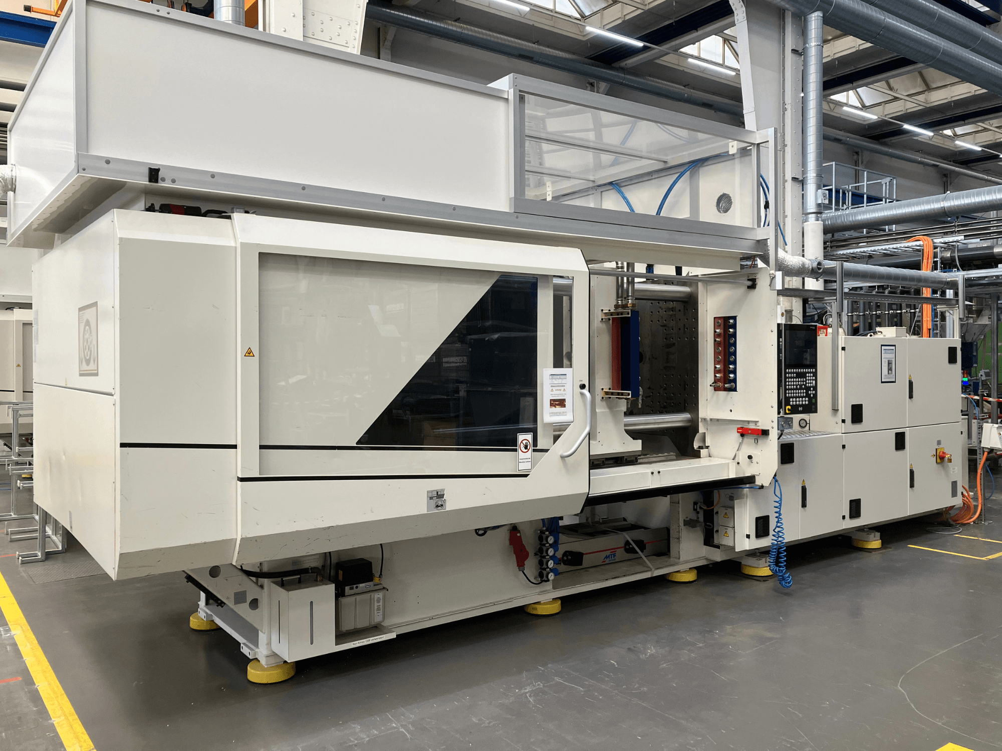 Вид сбоку на термопластавтомат модели AET с панелью управления и прозрачными крышками в промышленной обстановке.