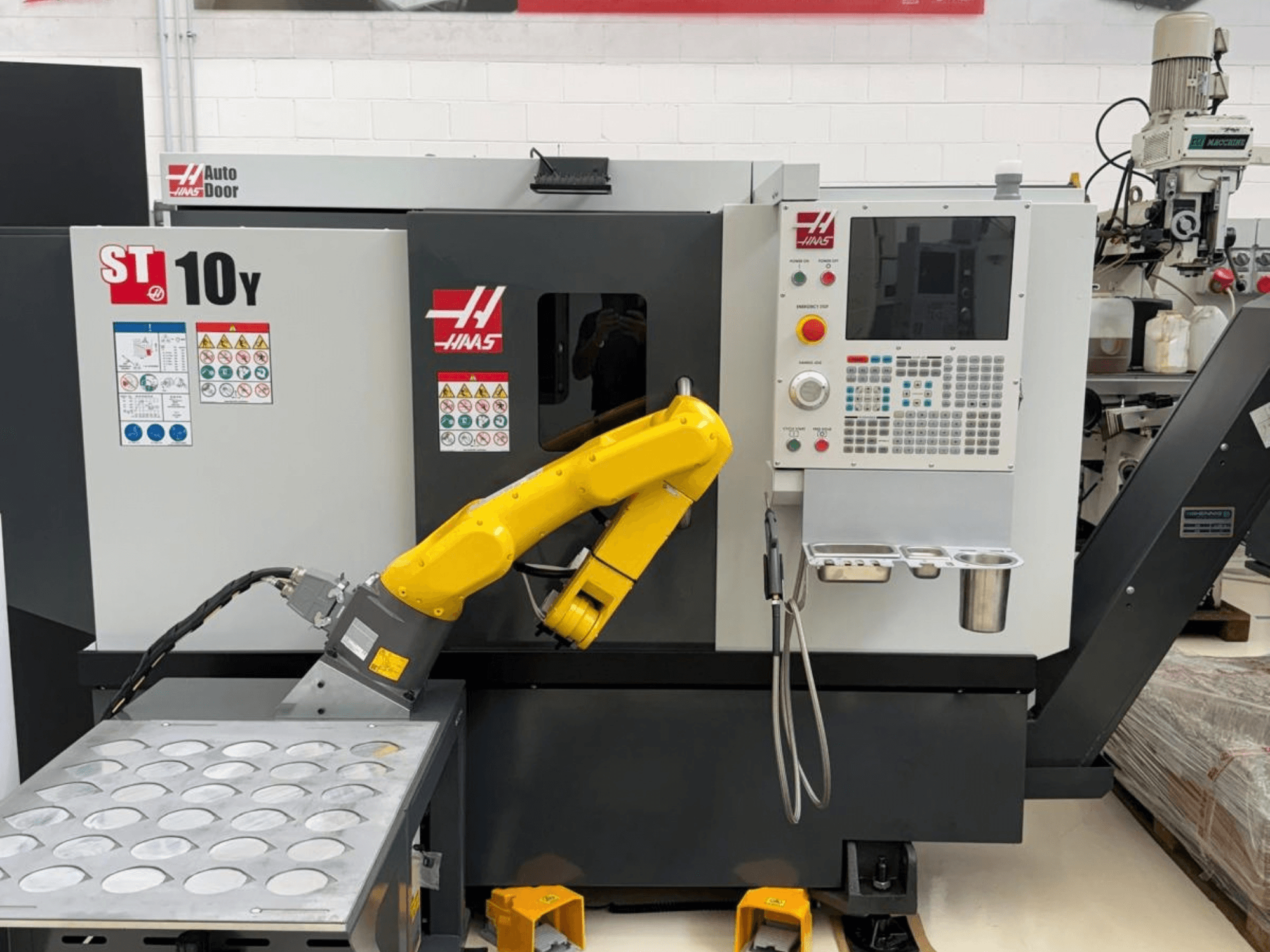 Горизонтальный токарный станок Haas ST-10Y, вид спереди, с роботизированным манипулятором и панелью управления с лотками для держателей инструментов.