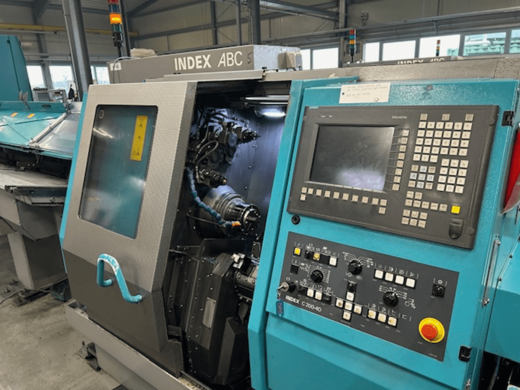 Вид спереди токарного станка с ЧПУ INDEX C200-AD с панелью управления, видимыми внутренними компонентами и элементами безопасности.