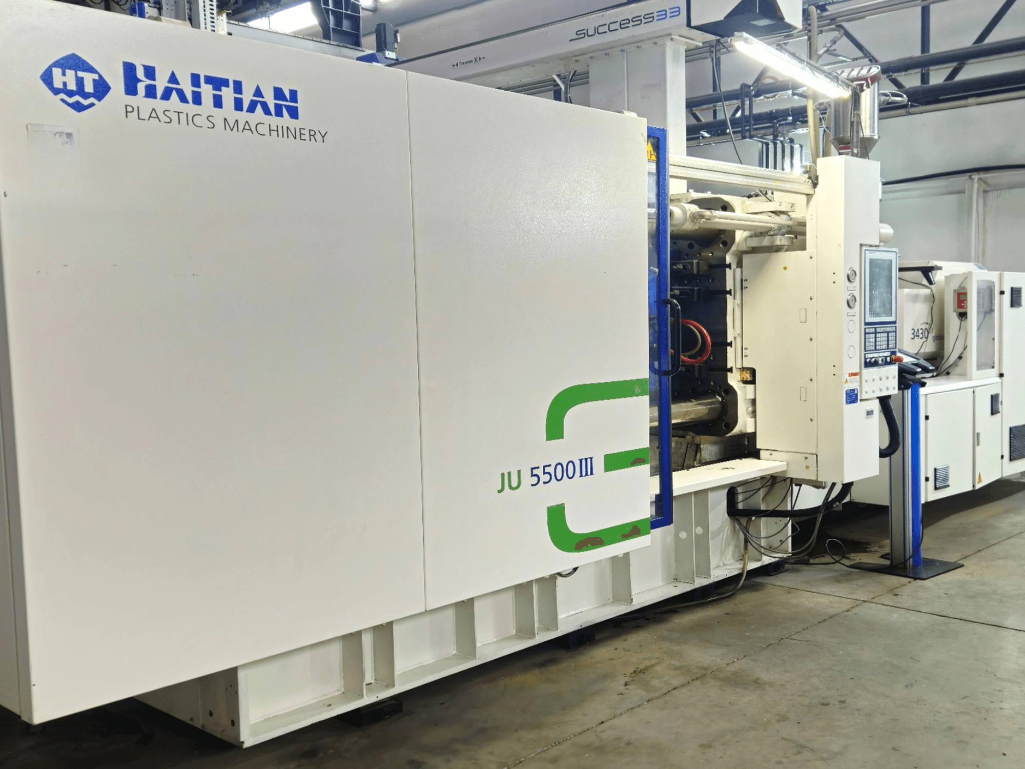 Гаитянское оборудование для производства пластмасс JU 5500III на заводе, вид спереди, демонстрирующий панель управления и производственную зону.