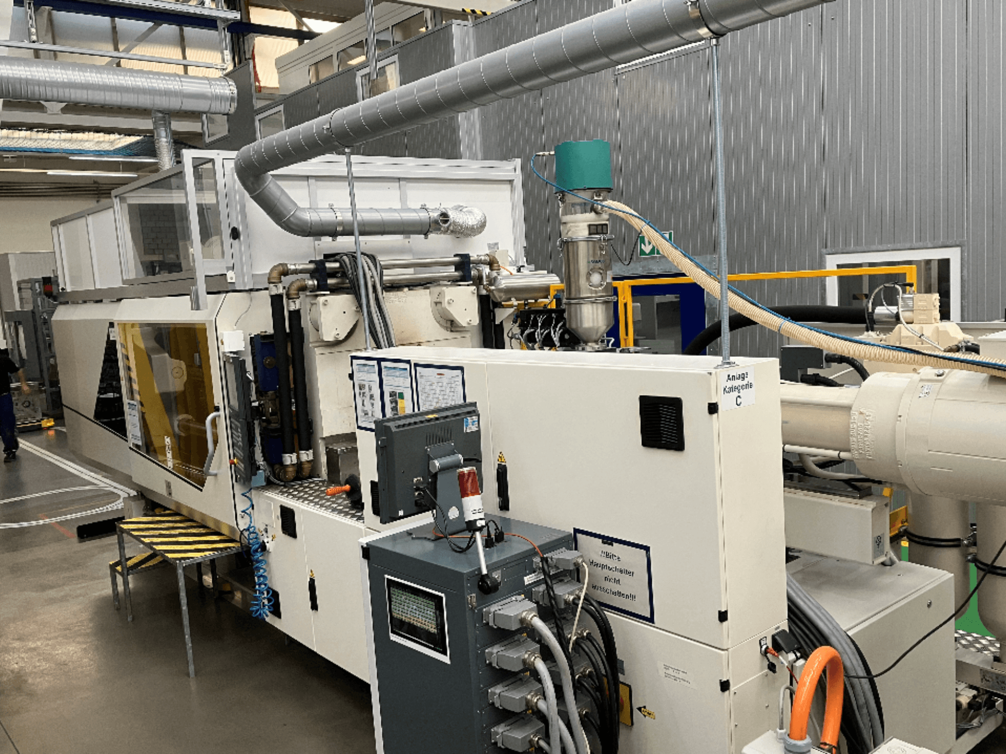 Машина для литья под давлением, вид спереди, с фирменной этикеткой, панелью управления и видимыми шлангами на заводе.