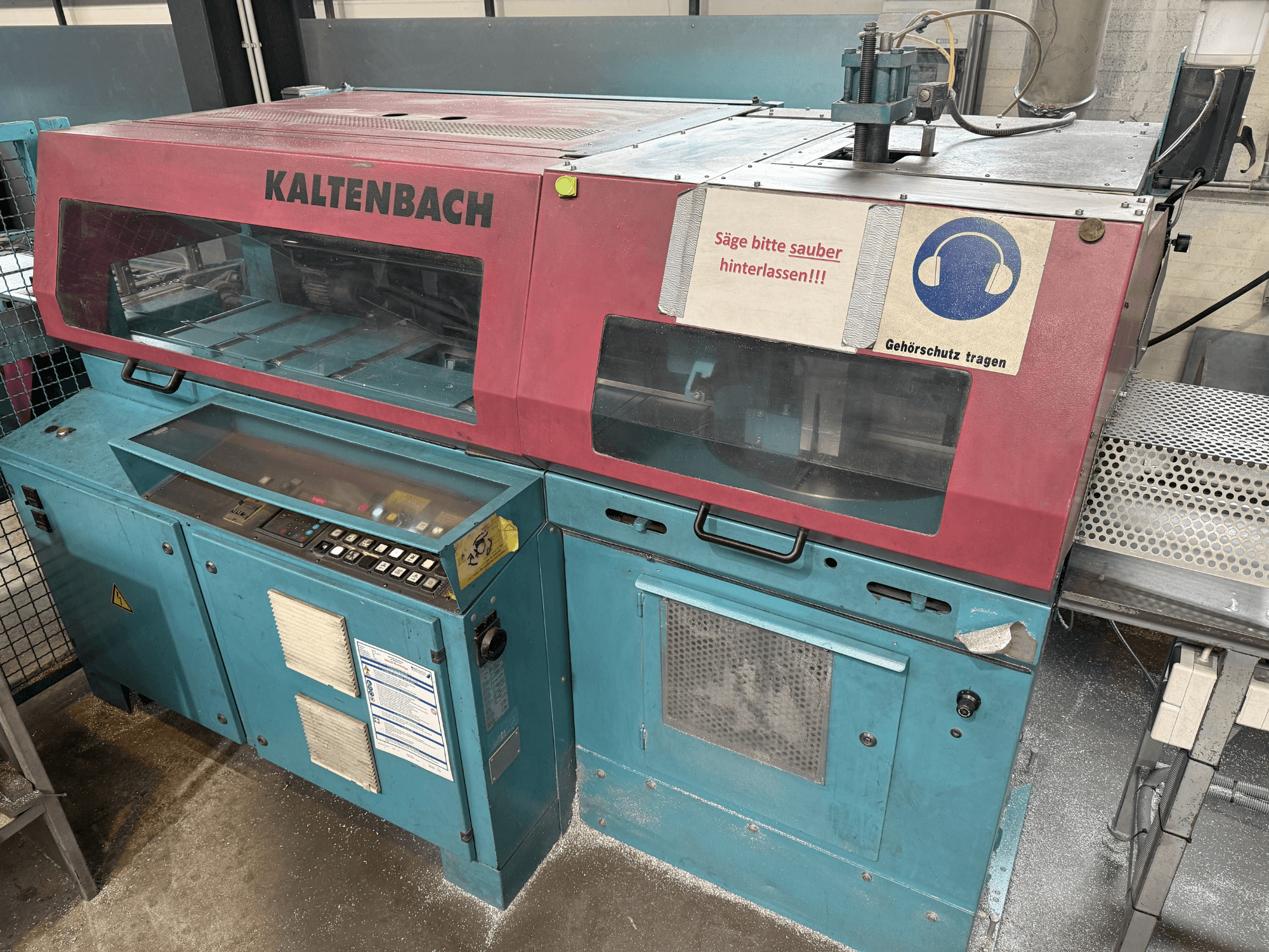 Промышленный режущий станок KALTENBACH, вид спереди, панель управления и знак безопасности для защиты органов слуха.