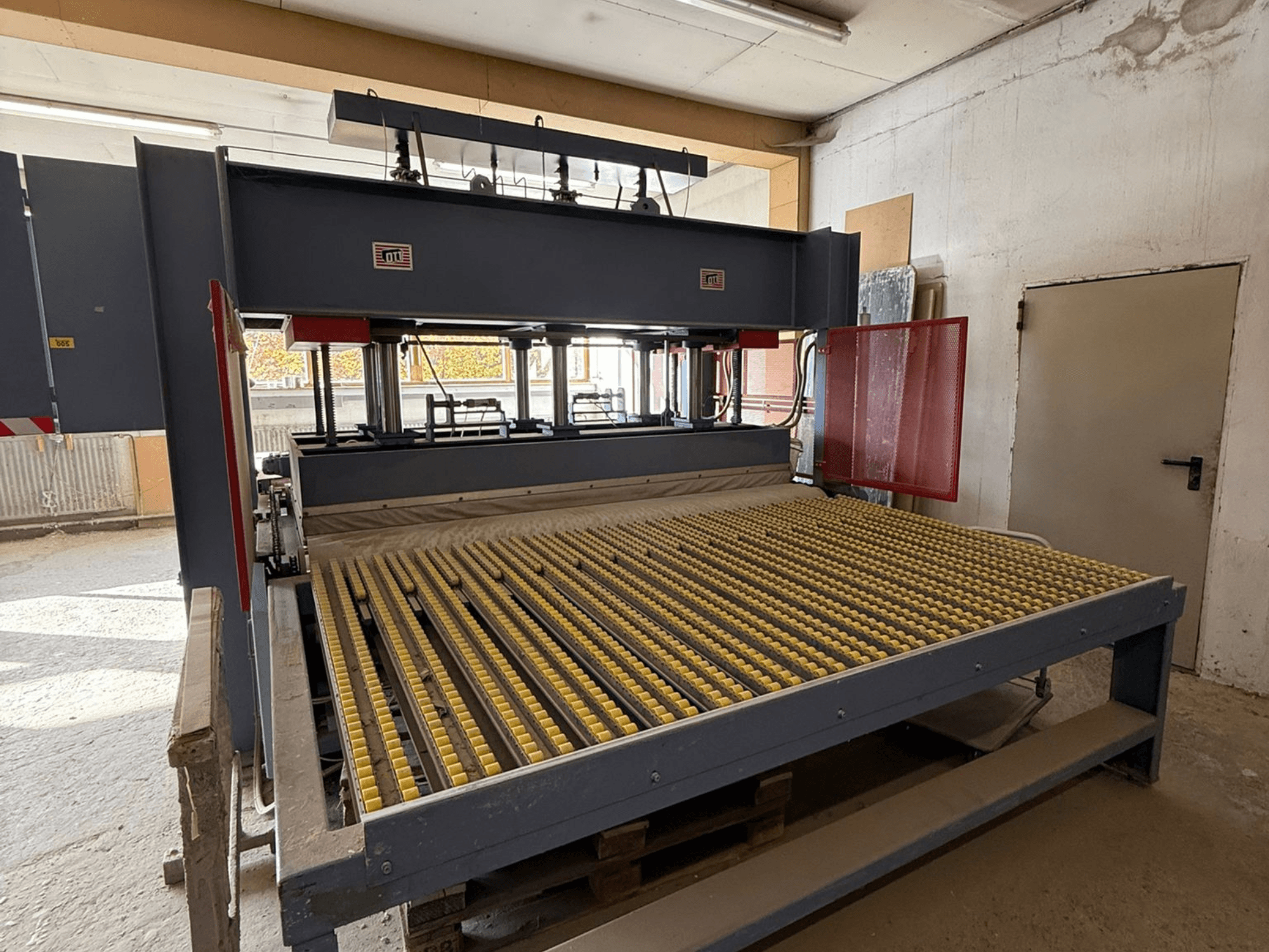 Промышленный станок с желтыми роликами, вид спереди, виден логотип бренда, используется для обработки материалов в мастерской.