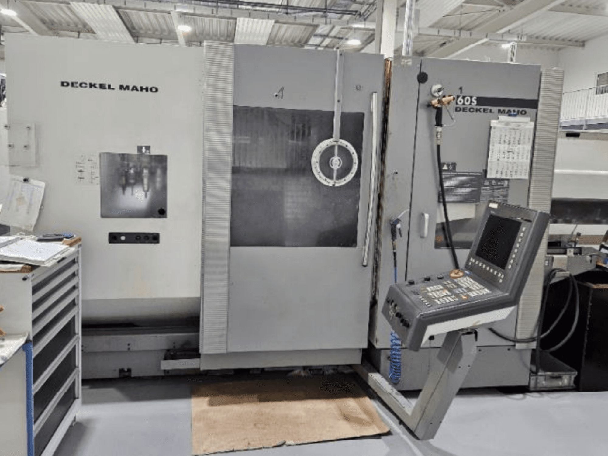 Вид спереди на станок с ЧПУ DECKEL MAHO 60S с панелью управления, видны инструменты, в мастерской.