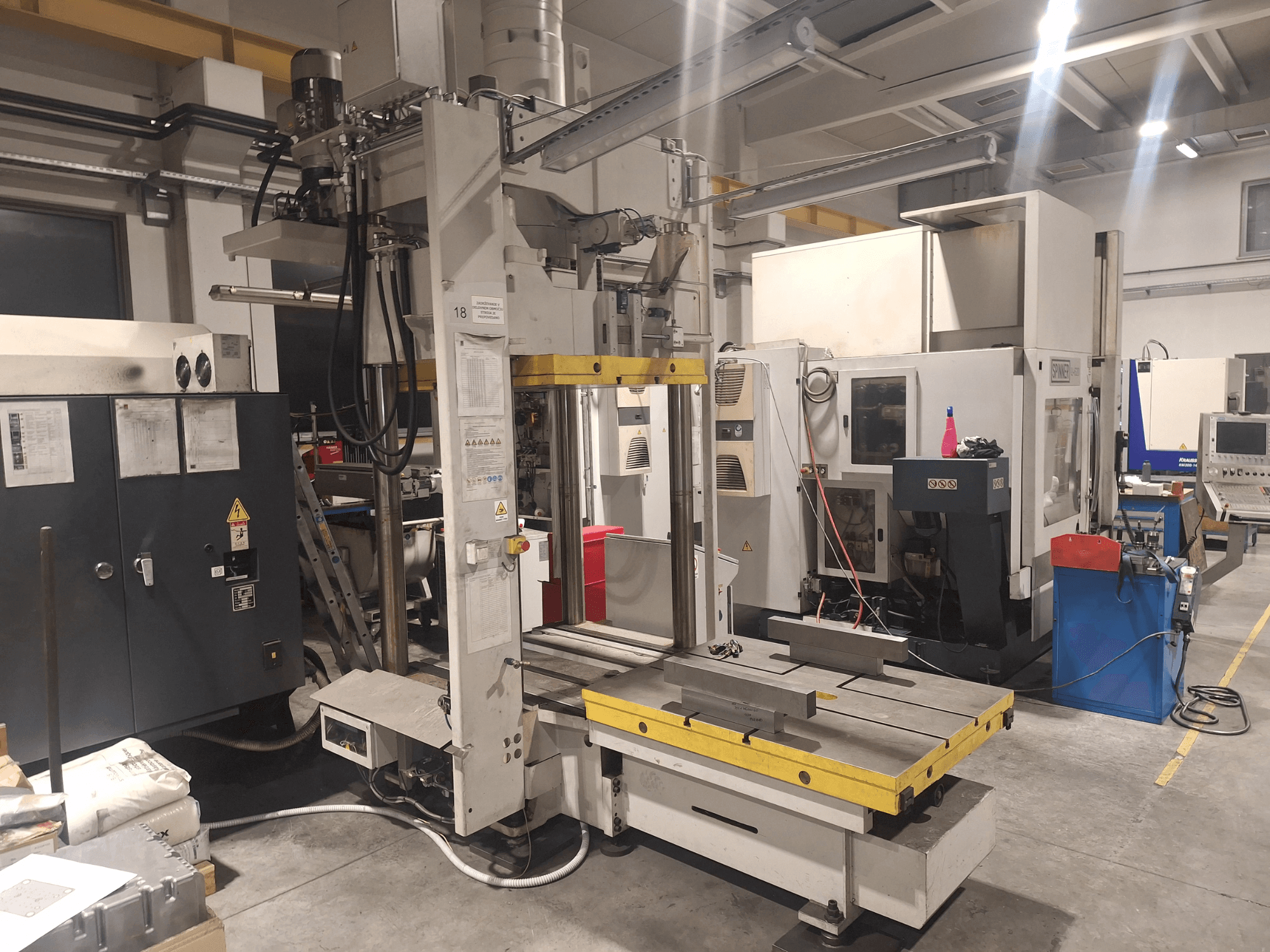 Горизонтально-фрезерный станок Synergic, вид спереди; широкий стол и различные панели управления, в мастерской.