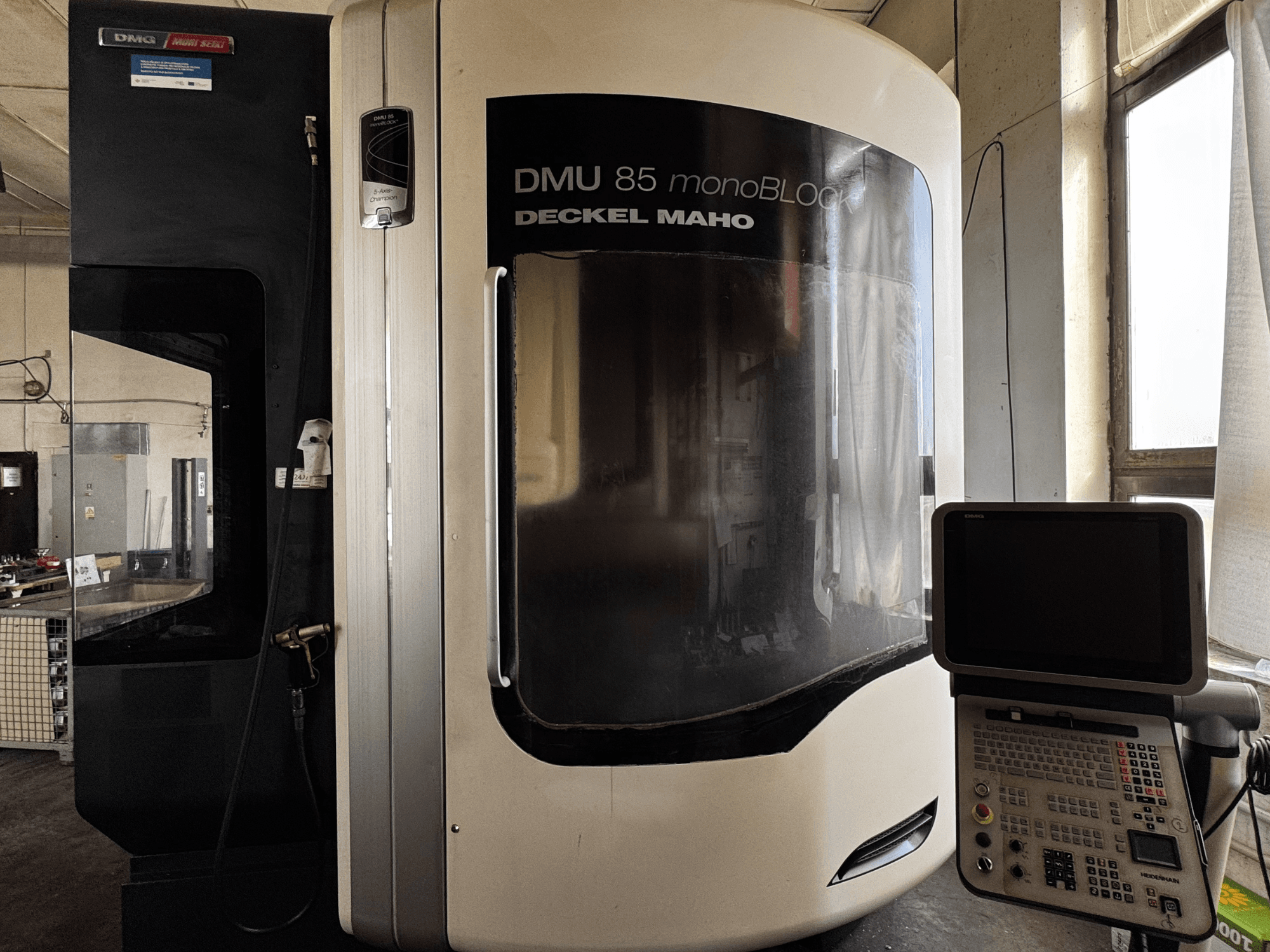 Вертикальный обрабатывающий центр DMG MORI DMU 85 monoBLOCK, вид спереди с панелью управления и большим смотровым окном.