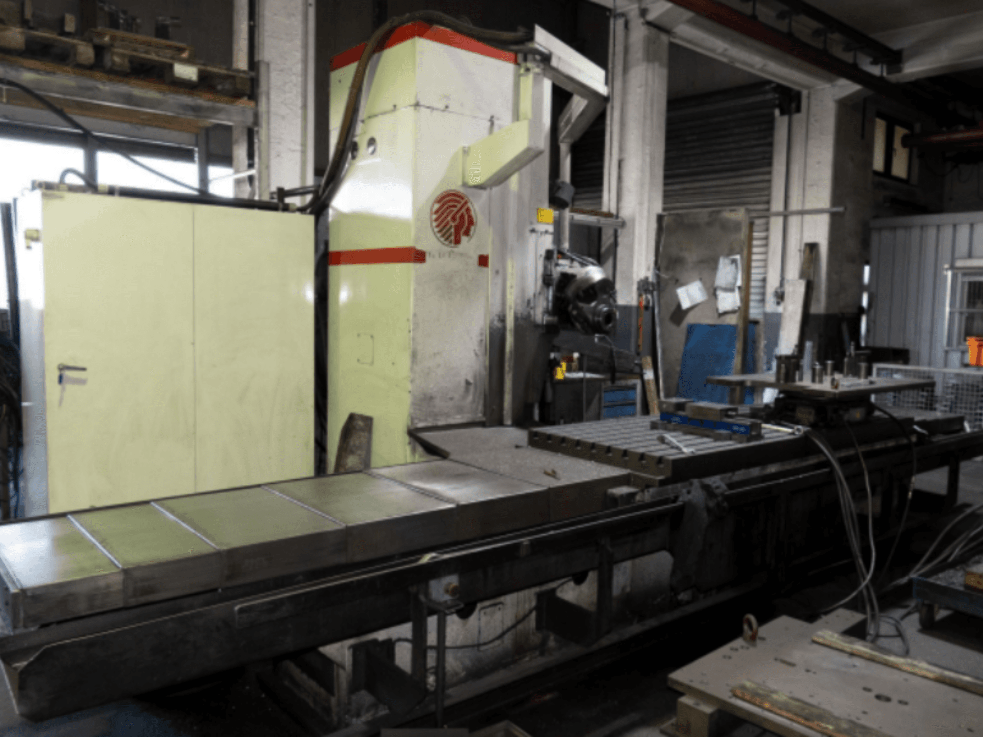 Промышленный фрезерный станок с большим столом, вид сбоку, демонстрирует органы управления и приспособления в мастерской.