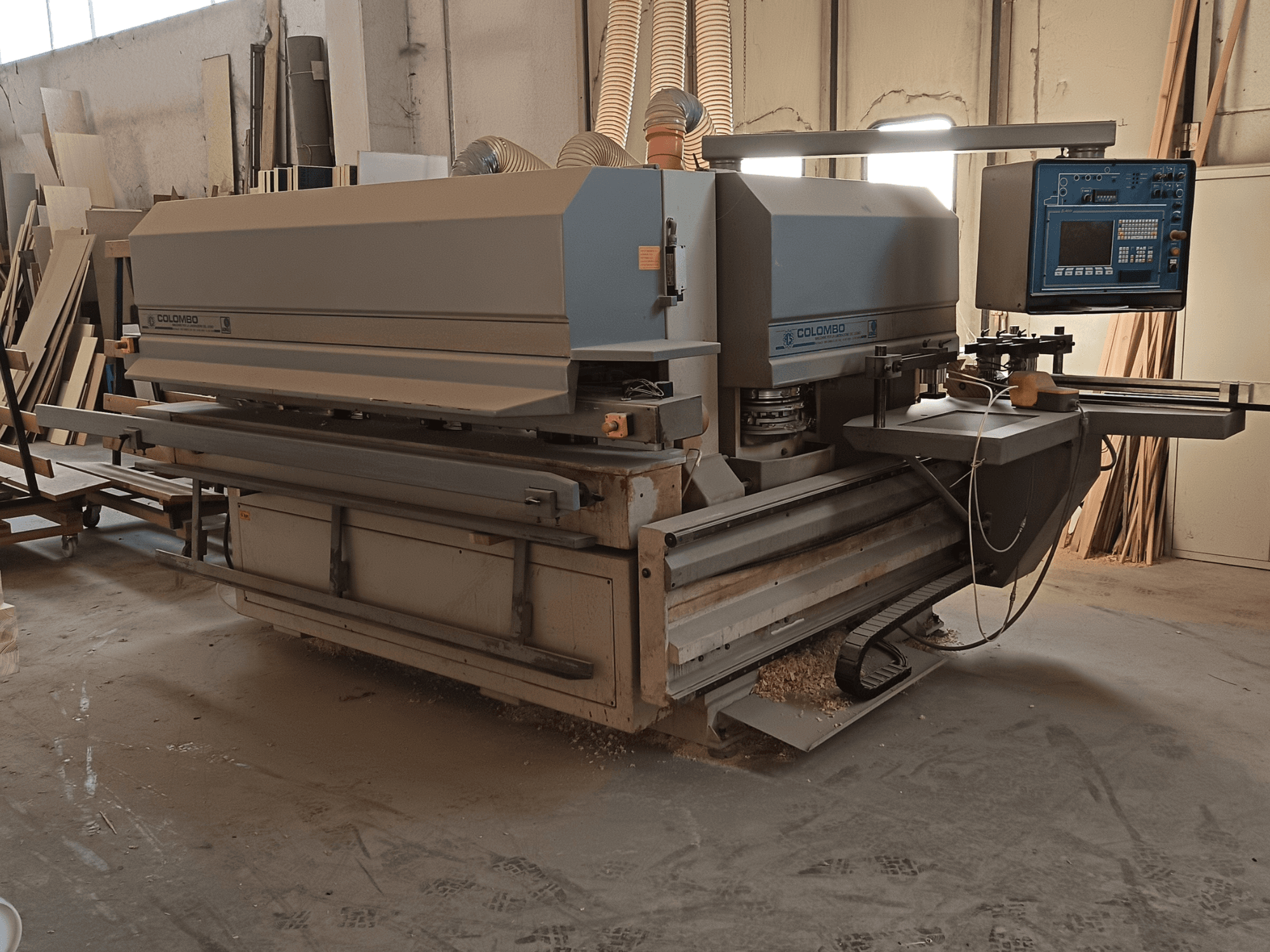 Деревообрабатывающий станок Colombo, вид сбоку, демонстрирует панель управления, режущие диски и скопление пильной пыли в мастерской.