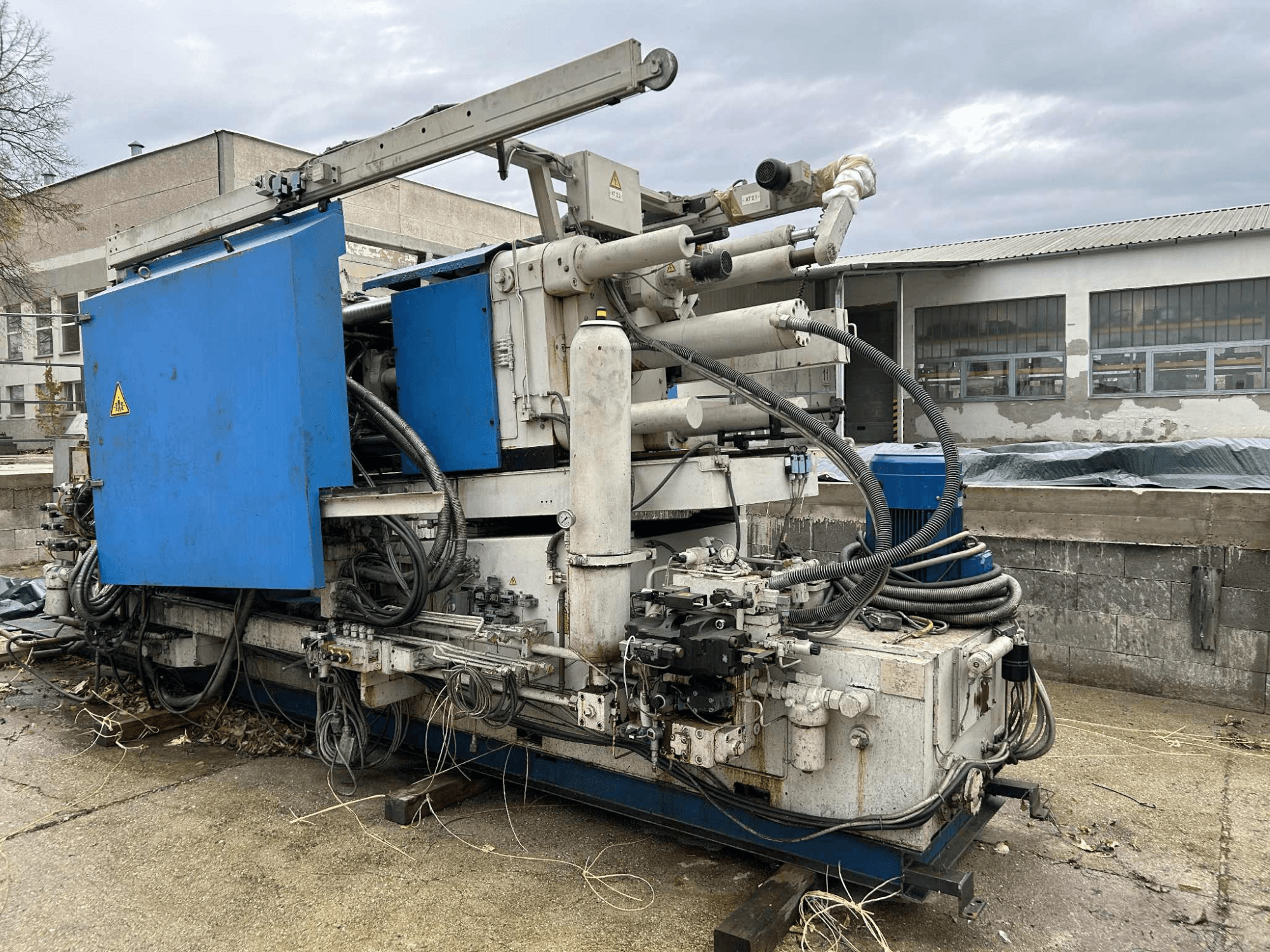 Большая промышленная гидравлическая машина с синим корпусом, различными шлангами и металлическими компонентами, вид сбоку.