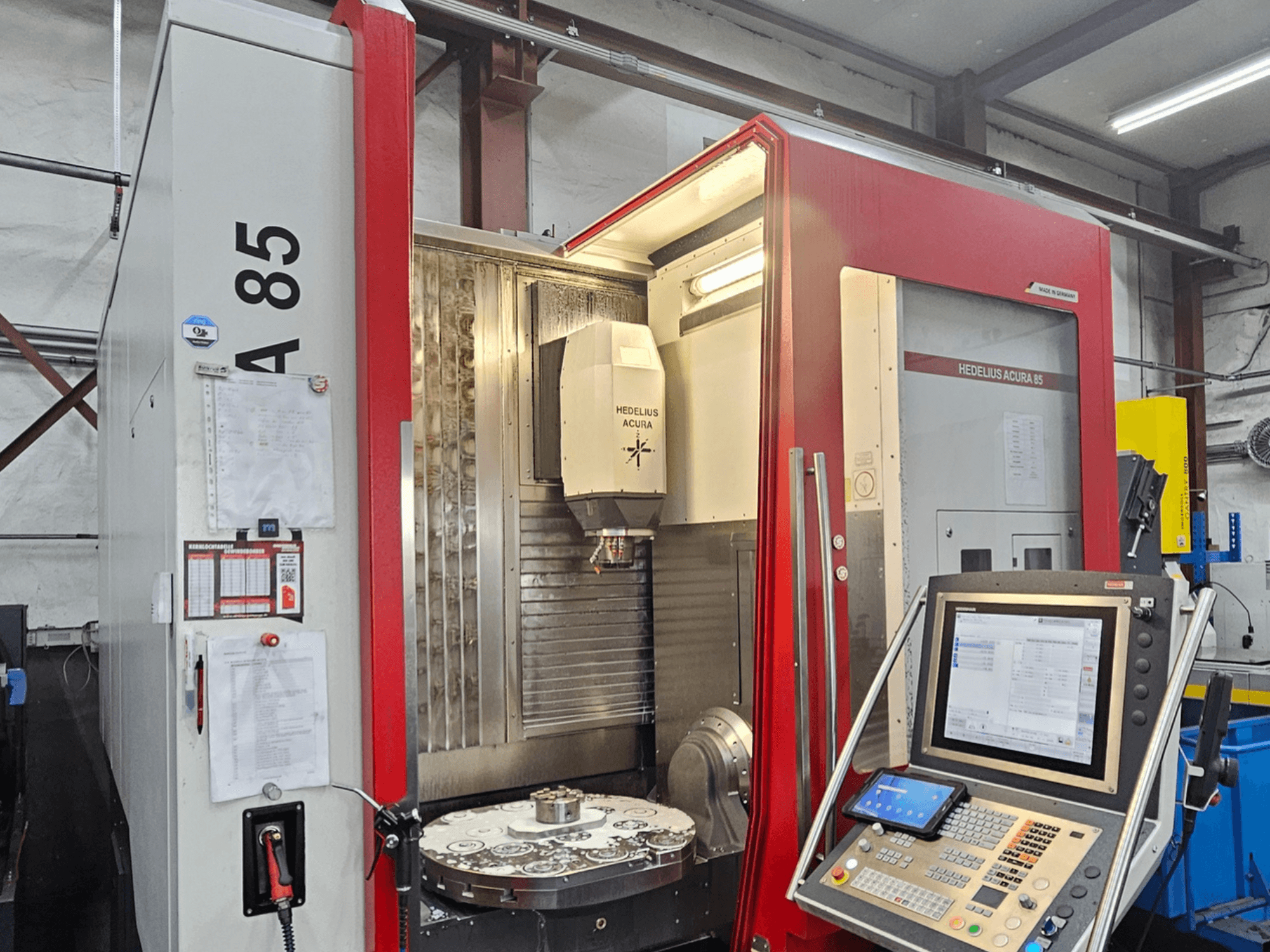 Вертикальный обрабатывающий центр HEDLIUS Acura 85, вид спереди, оснащен панелью управления и вращающимся столом для точной обработки.