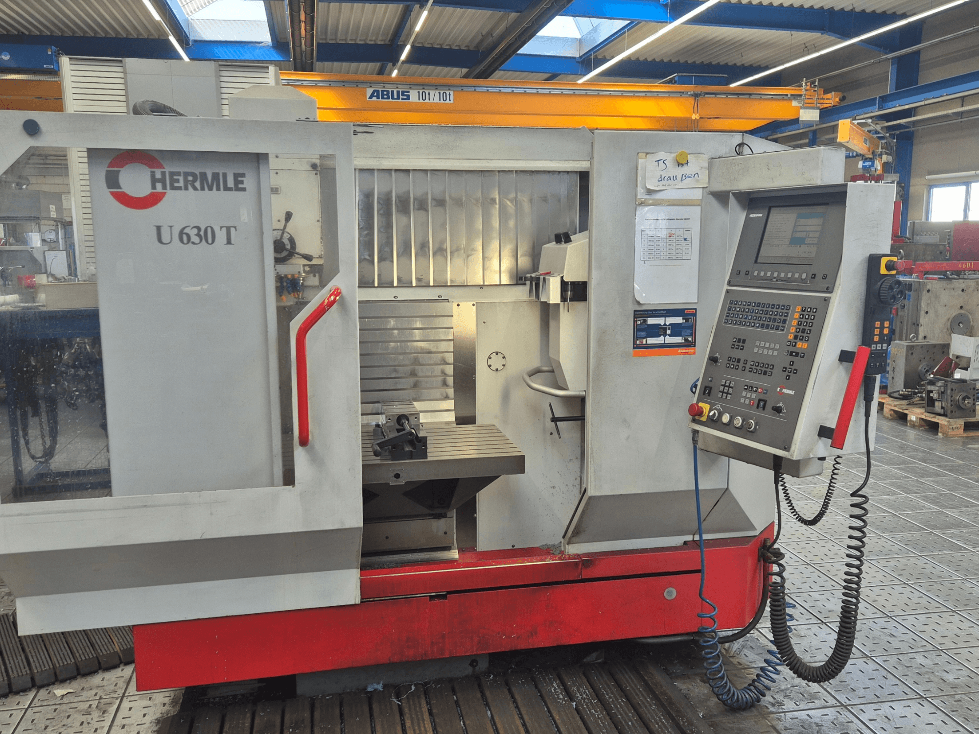 Вертикальный обрабатывающий центр HERMLE U 630 T с видом спереди, панель управления, рабочий стол и защитное ограждение.