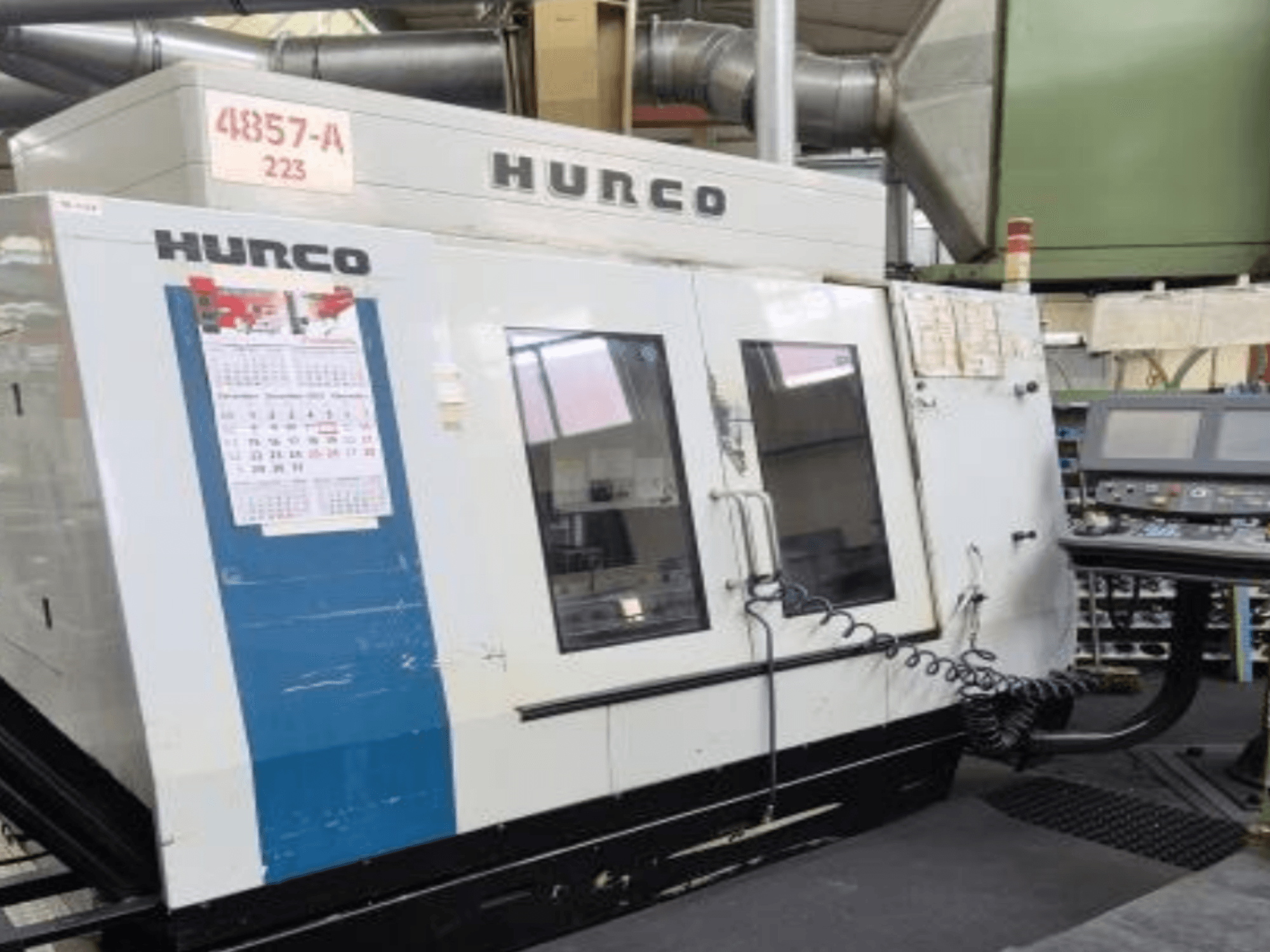 Вертикальный обрабатывающий центр Hurco VMX 42 с видом спереди, с панелью управления, календарем и внешними металлическими деталями.