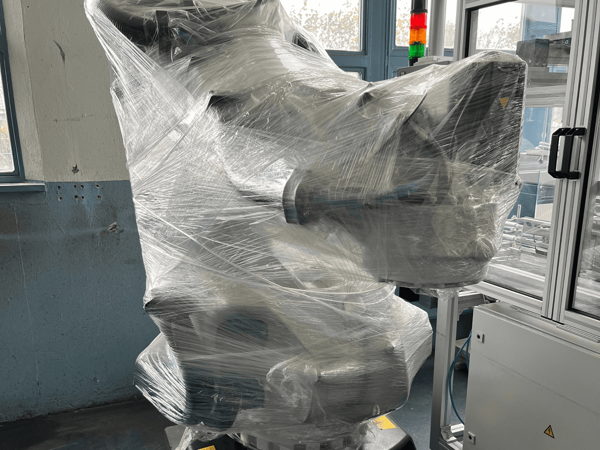 Промышленный роботизированный манипулятор в пластиковой упаковке, вид спереди. Включает блок управления и индикатор. Бренд не виден.