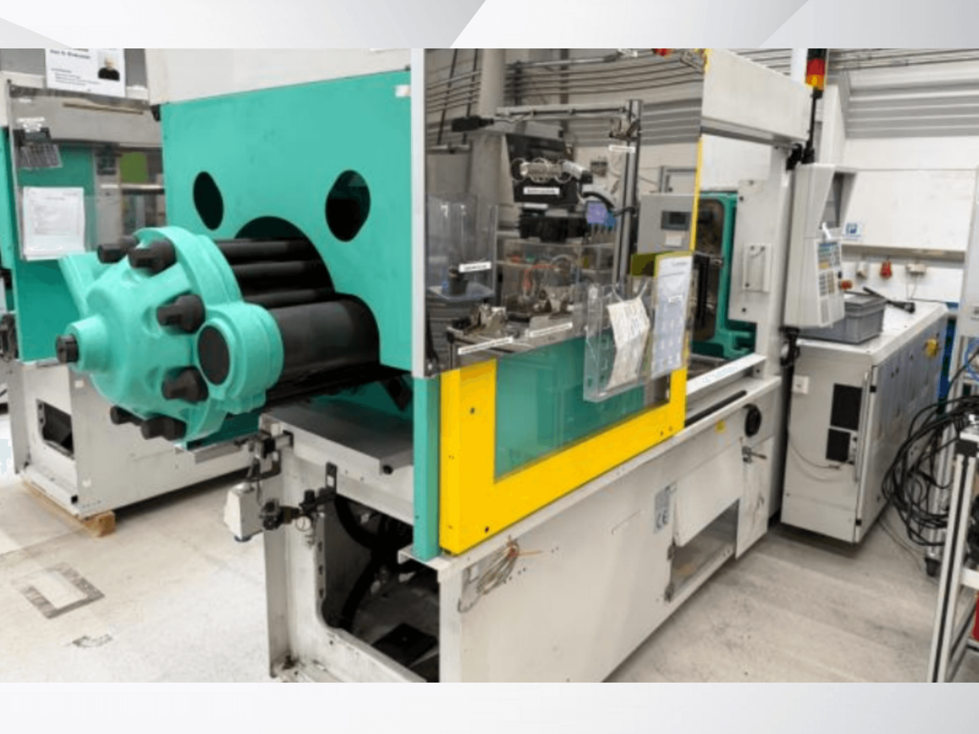 Машина для литья под давлением, светло-голубая и желтая, вид спереди, с видимой пресс-формой и панелью управления с наклейками.