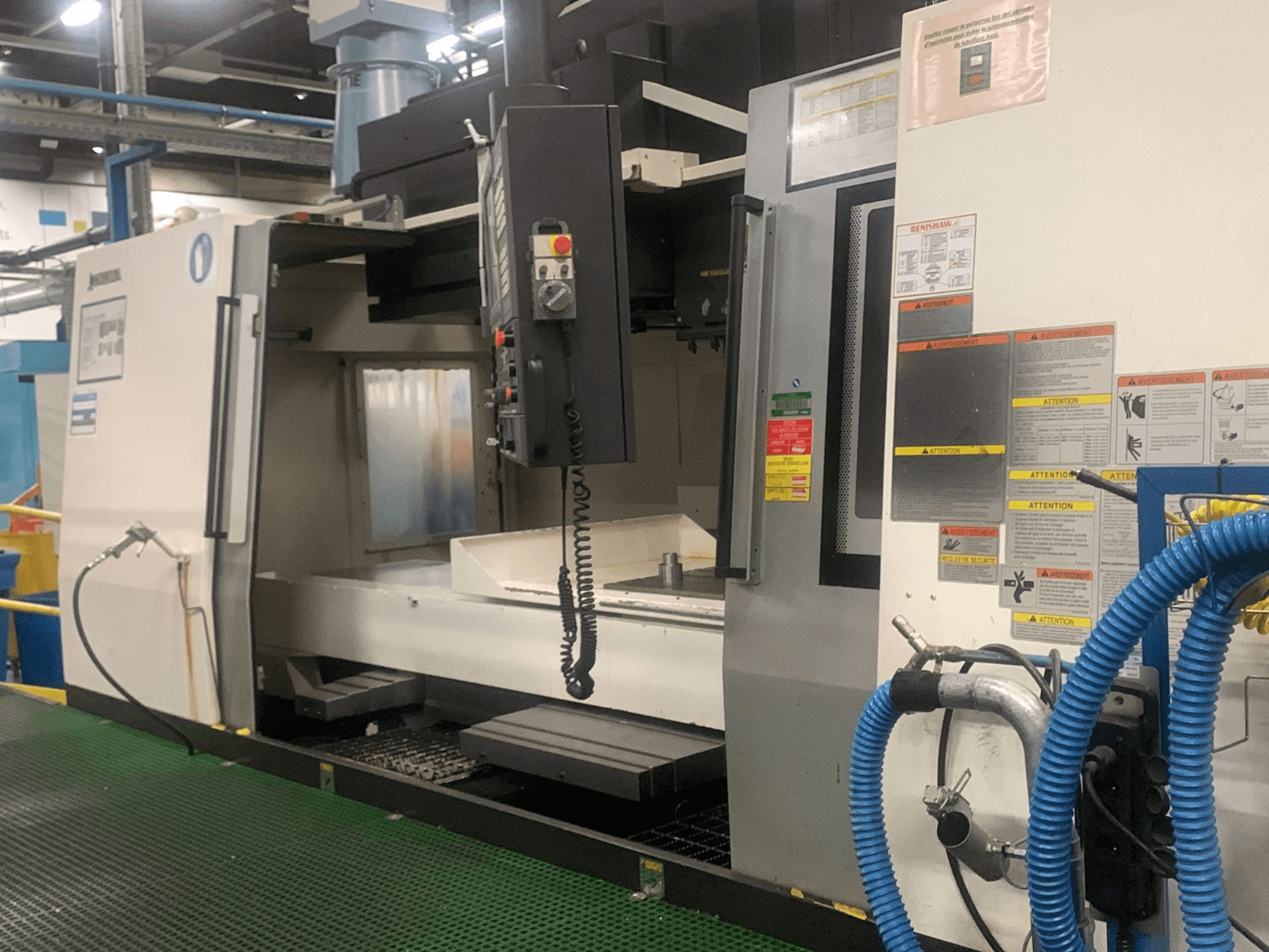 Вертикальный обрабатывающий центр Okuma Millac 852 VII, вид спереди, на котором видны панель управления, зона шпинделя и предупреждающие надписи.
