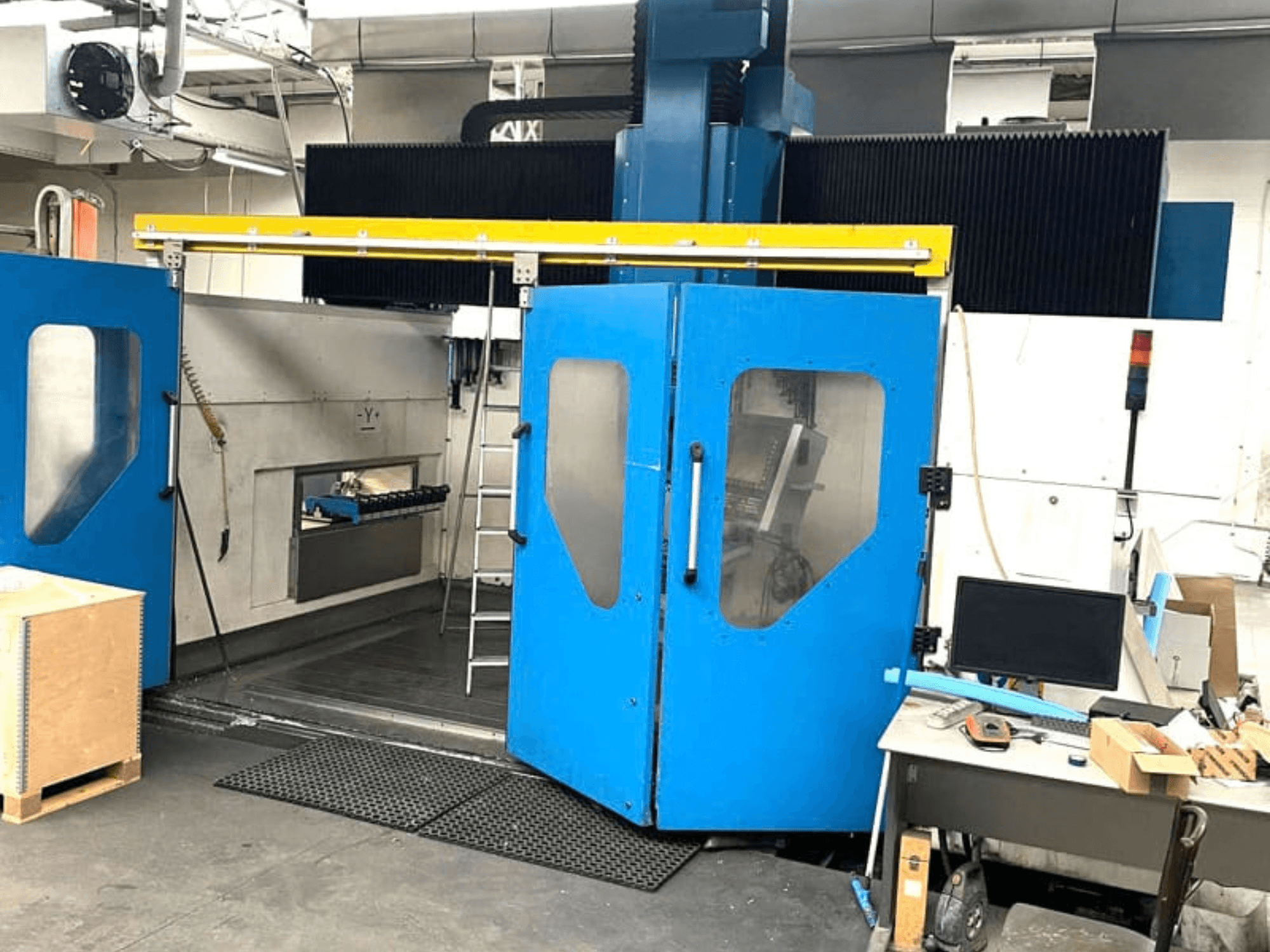 Вид спереди на вертикальный обрабатывающий центр TECHMILL LABOR SHAPE 3220 с открытыми синими дверцами, за которыми видна рабочая зона внутри.