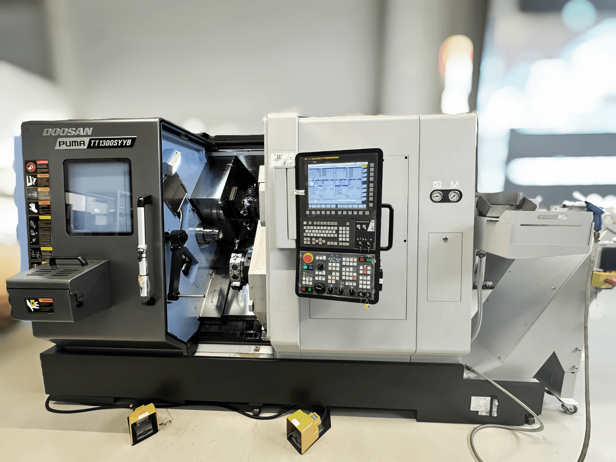 Токарно-фрезерный центр Doosan Puma TT1300SYYB вид сбоку, демонстрирует панель управления и внутреннее устройство станка с видимыми инструментами.