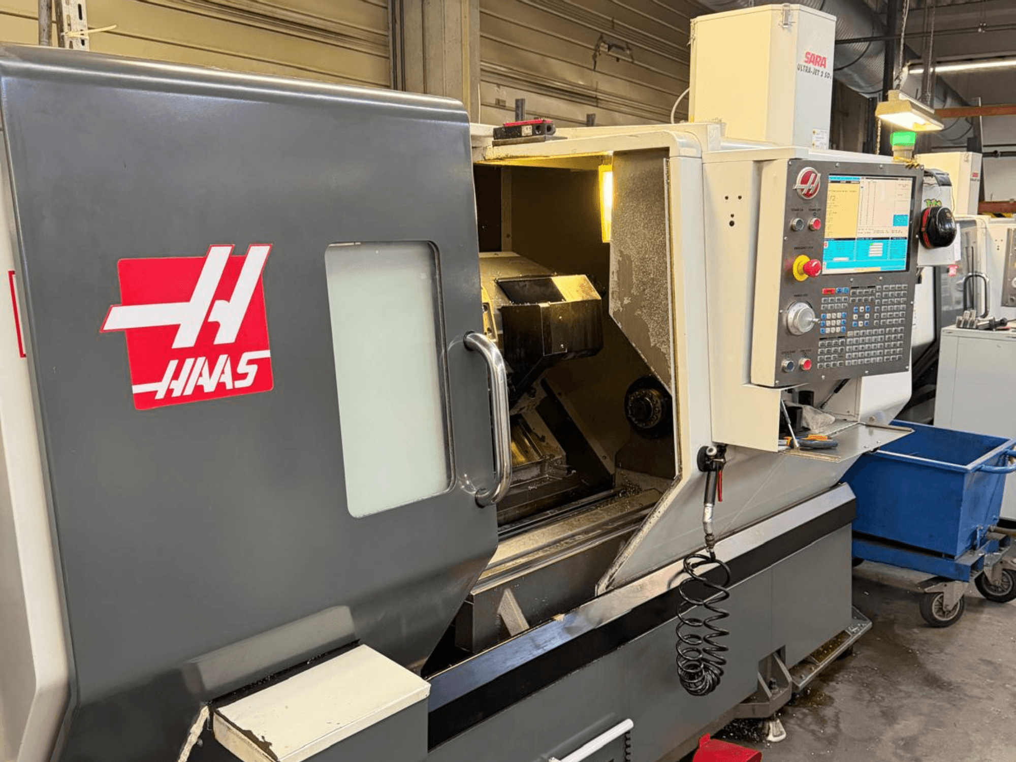 Горизонтальный токарный станок HAAS DS-30SSY, вид спереди, видна панель управления и внутренние компоненты, в мастерской.