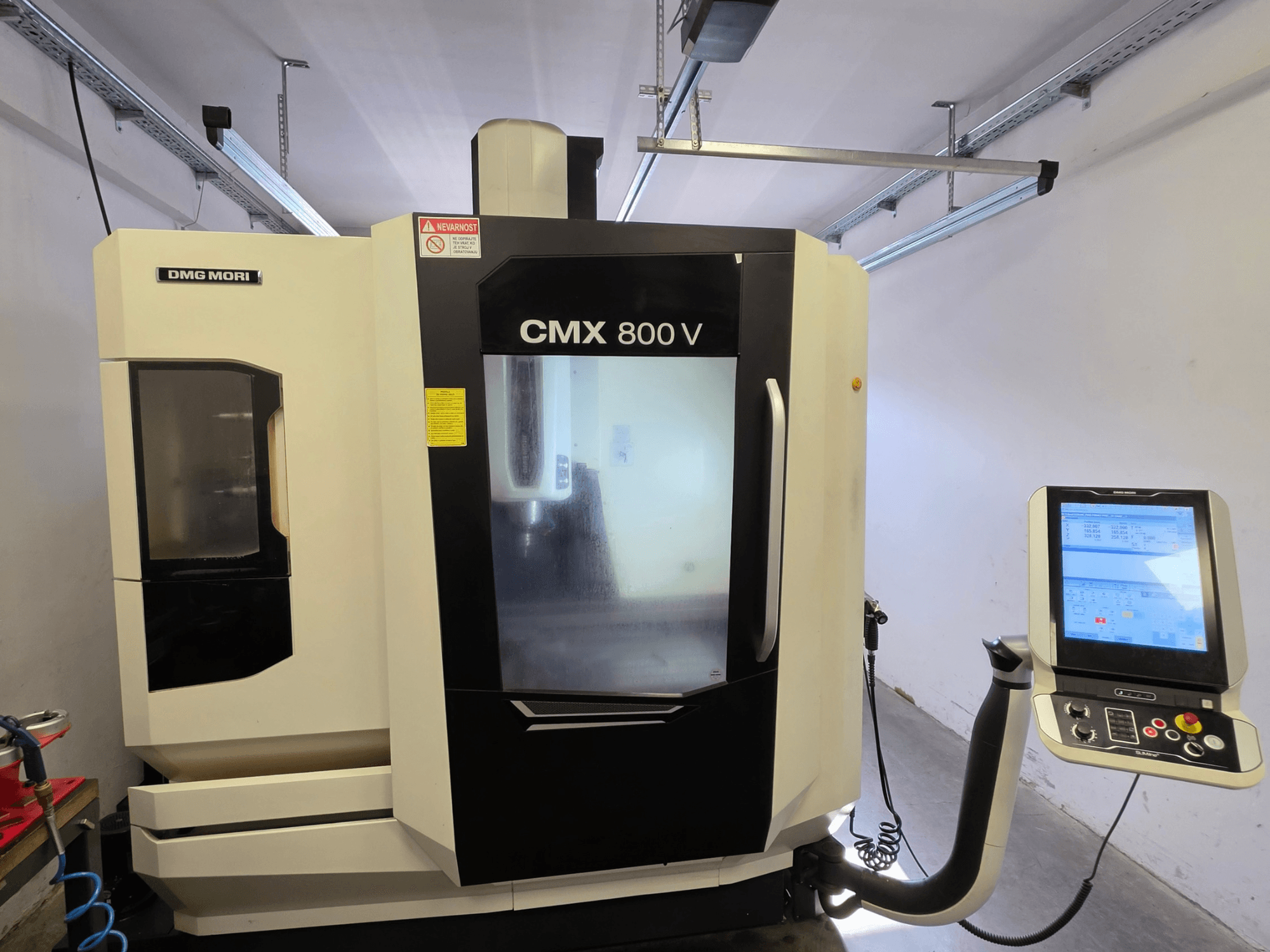 Вертикальный обрабатывающий центр DMG MORI CMX 800V, вид спереди, с сенсорной панелью управления и четкими знаками безопасности.
