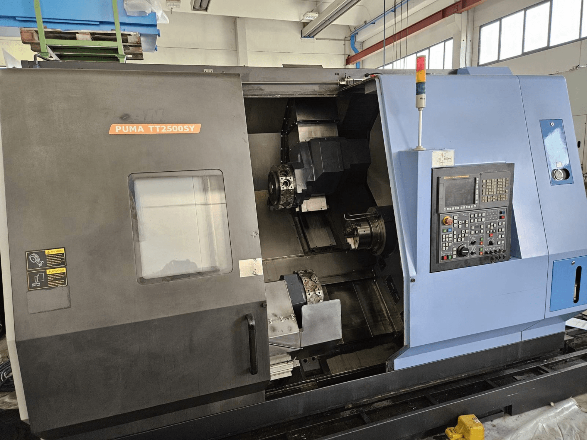 Многошпиндельный токарный станок DOOSAN PUMA TT2500SY, вид спереди с панелью управления и деталями внутренней конструкции станка.