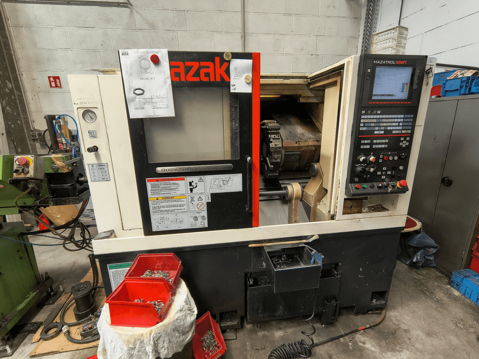 Mazak Quick Turn Smart 100 S, вид сбоку, на котором видны панель управления, поддон для охлаждающей жидкости и ящики для хранения с винтами.