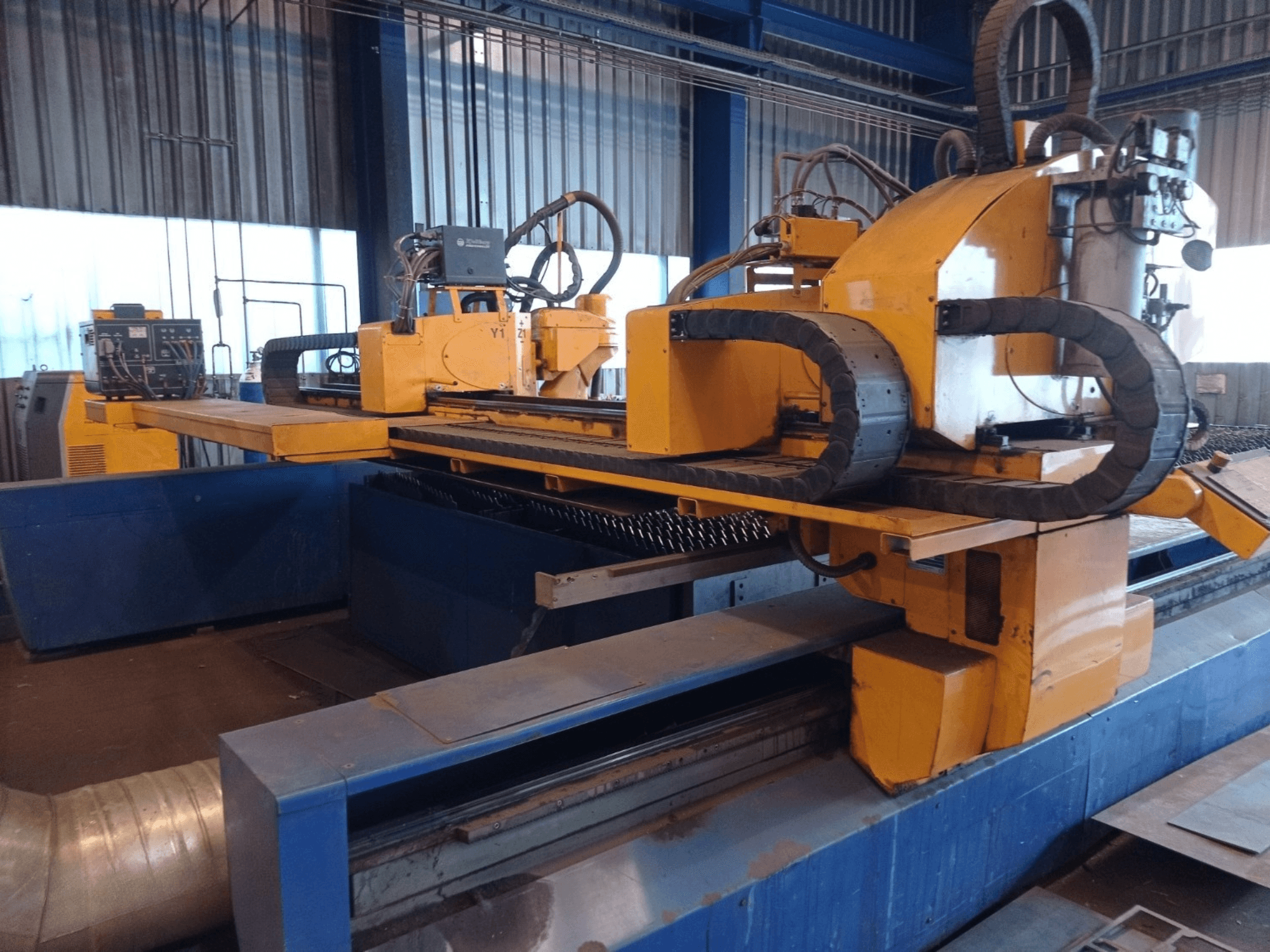 Желтый станок плазменной резки с ЧПУ с двумя горизонтальными рычагами, показанный спереди, с панелью управления и режущей станиной.