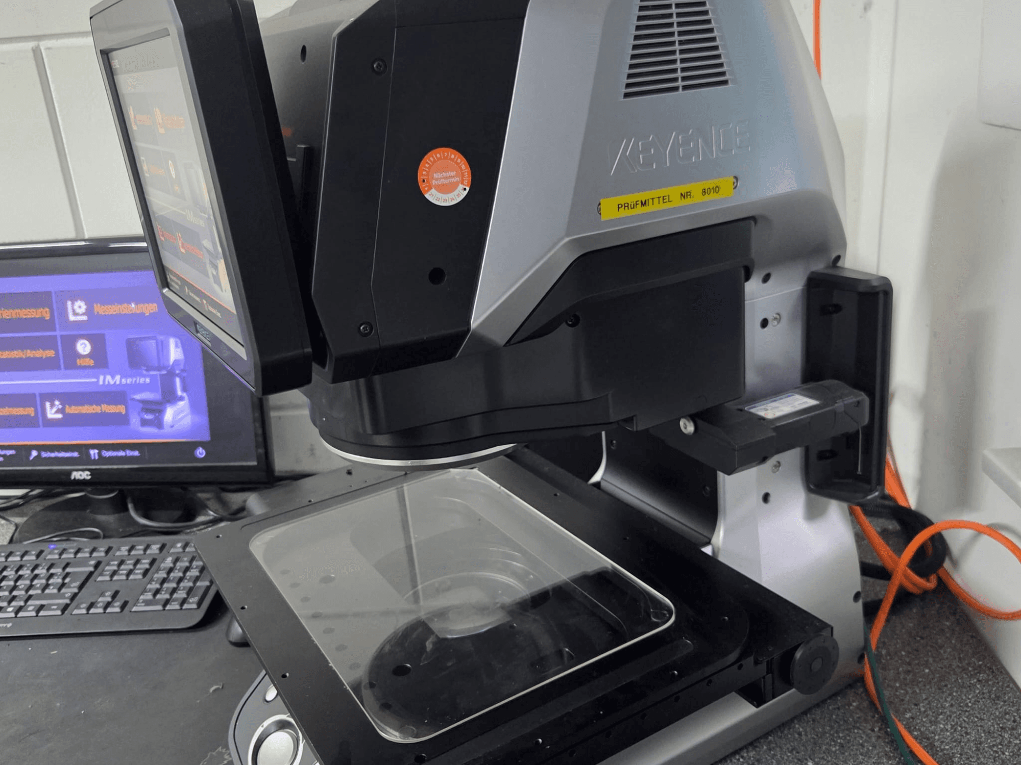 Оптическая измерительная машина KEYENCE IM 7030, вид спереди с сенсорным дисплеем и стеклянной измерительной пластиной.