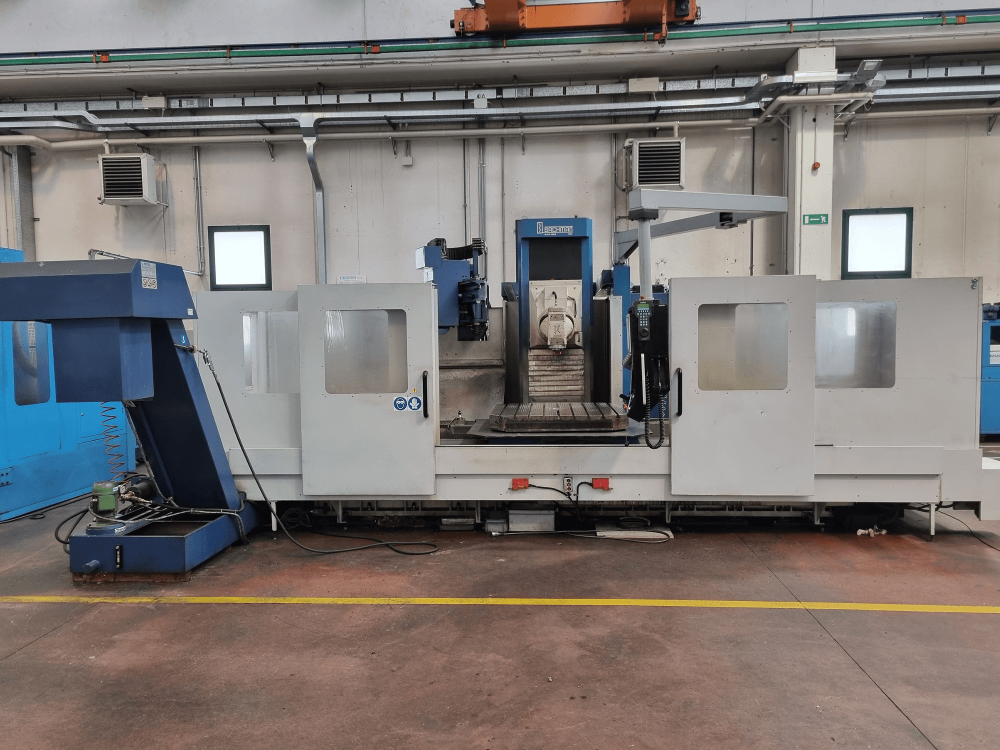 Фрезерный станок с ЧПУ фирмы "Brembana", вид сбоку, показывающий панель управления и рабочую зону с рабочим столом внутри.