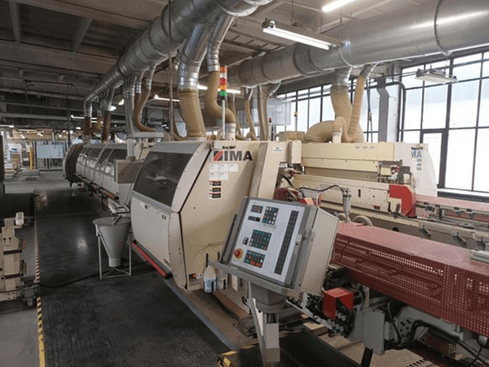 Промышленное оборудование IMA в заводских условиях, вид спереди, с панелями управления и трубами для удаления пыли.