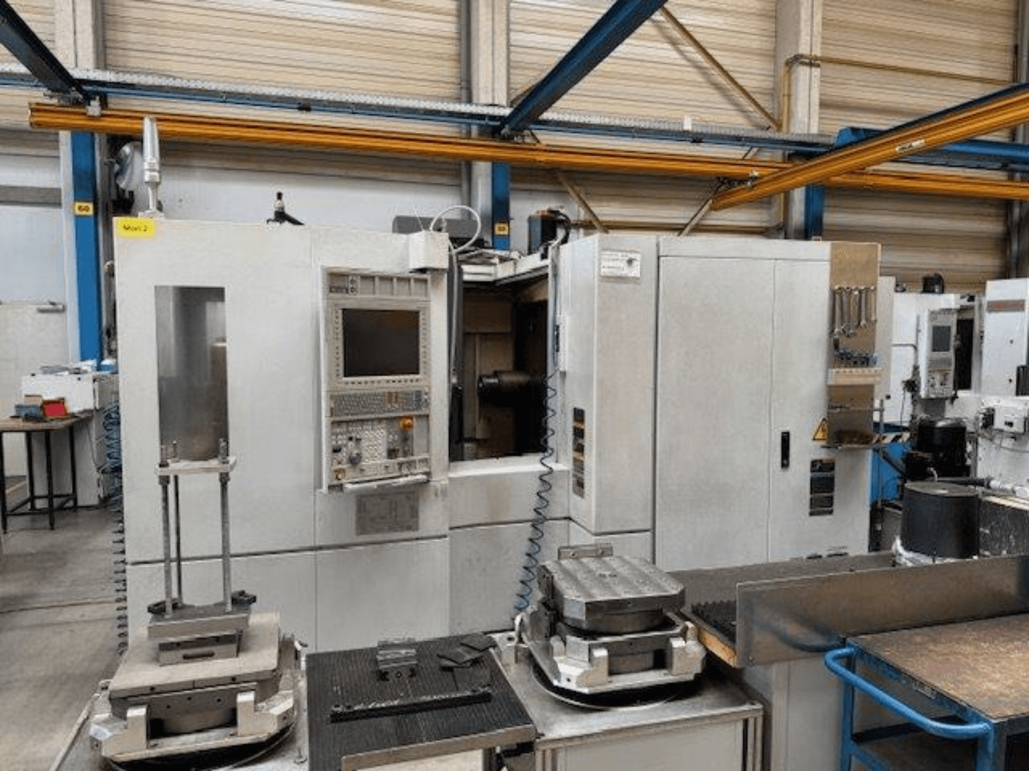 Вид спереди горизонтального обрабатывающего центра MORI SEIKI NH4000 DCG с панелью управления и заготовками на столе.
