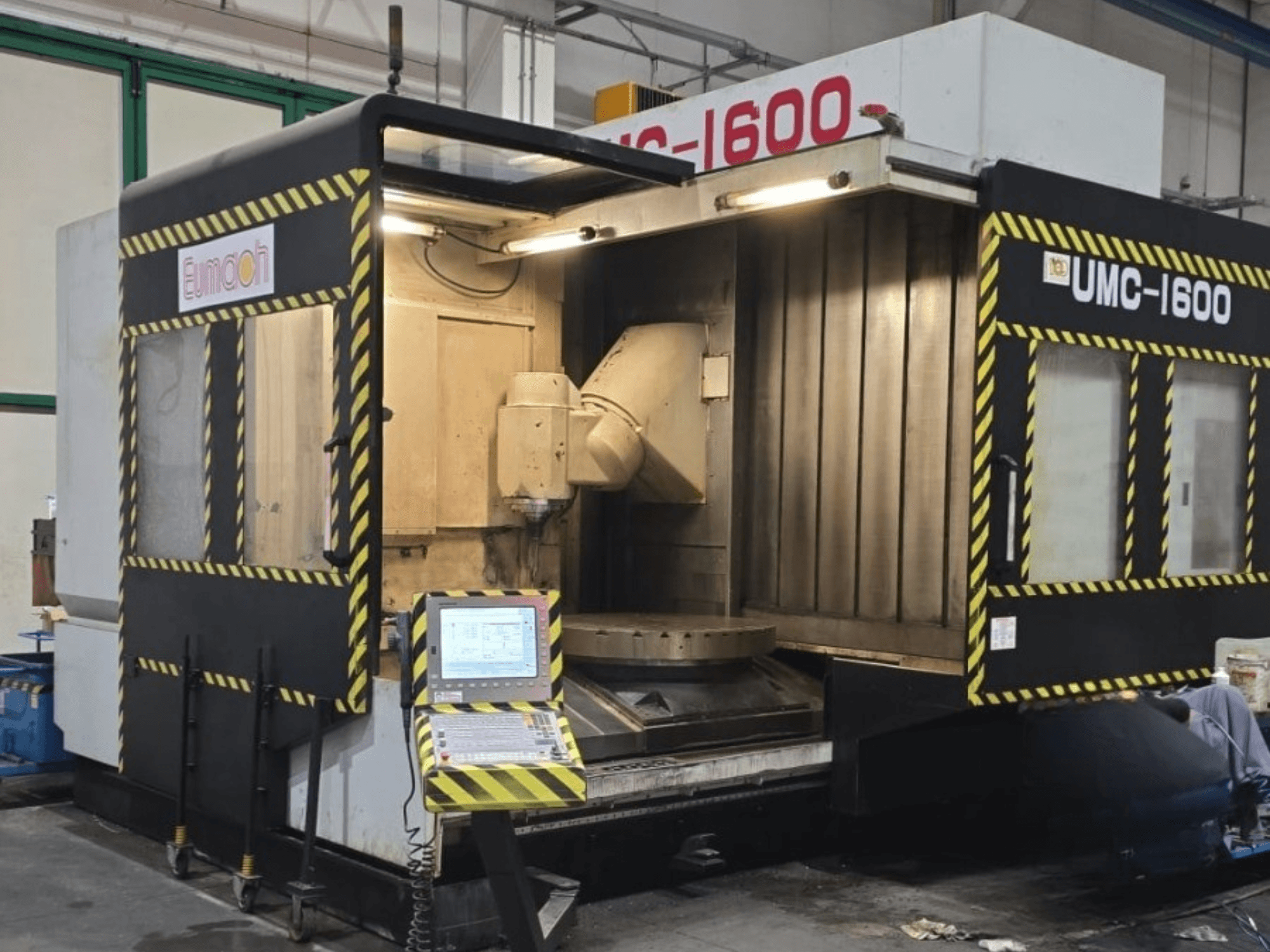 Вертикальный обрабатывающий центр Eumach UMC-1600, вид спереди с изображением органов управления и зоны обработки с сигнальными полосами.