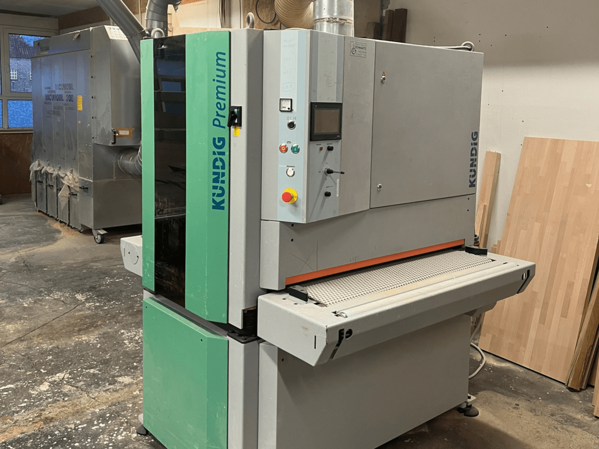 Ленточная шлифовальная машина Kundig Premium-1 1100K серо-зеленого цвета, вид сбоку с панелью управления и шлифовальной лентой.