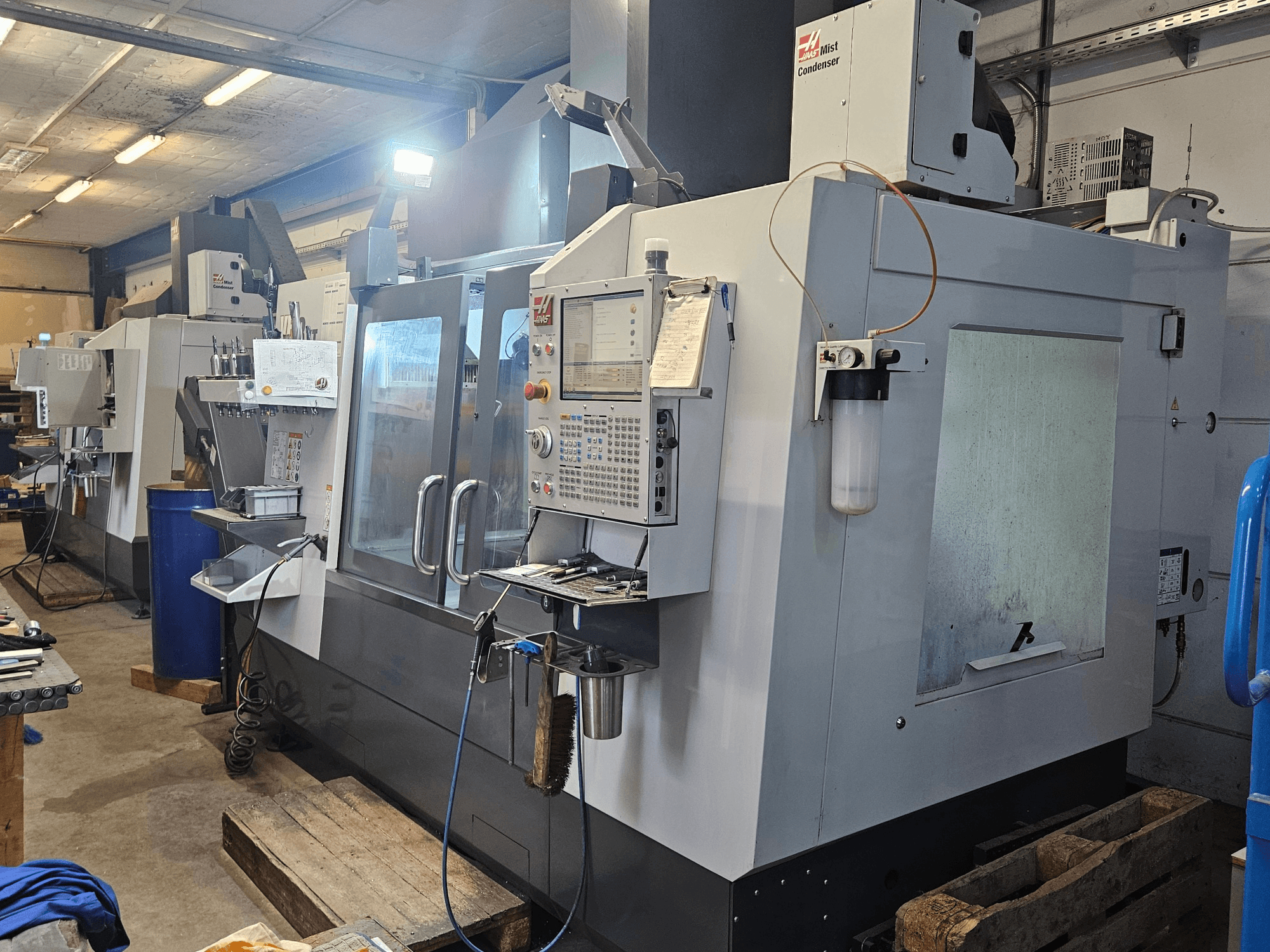 Вертикальный обрабатывающий центр Haas VF-3YT/50 в цехе, вид спереди, на котором видны панель управления, держатели инструментов и конденсатор тумана.